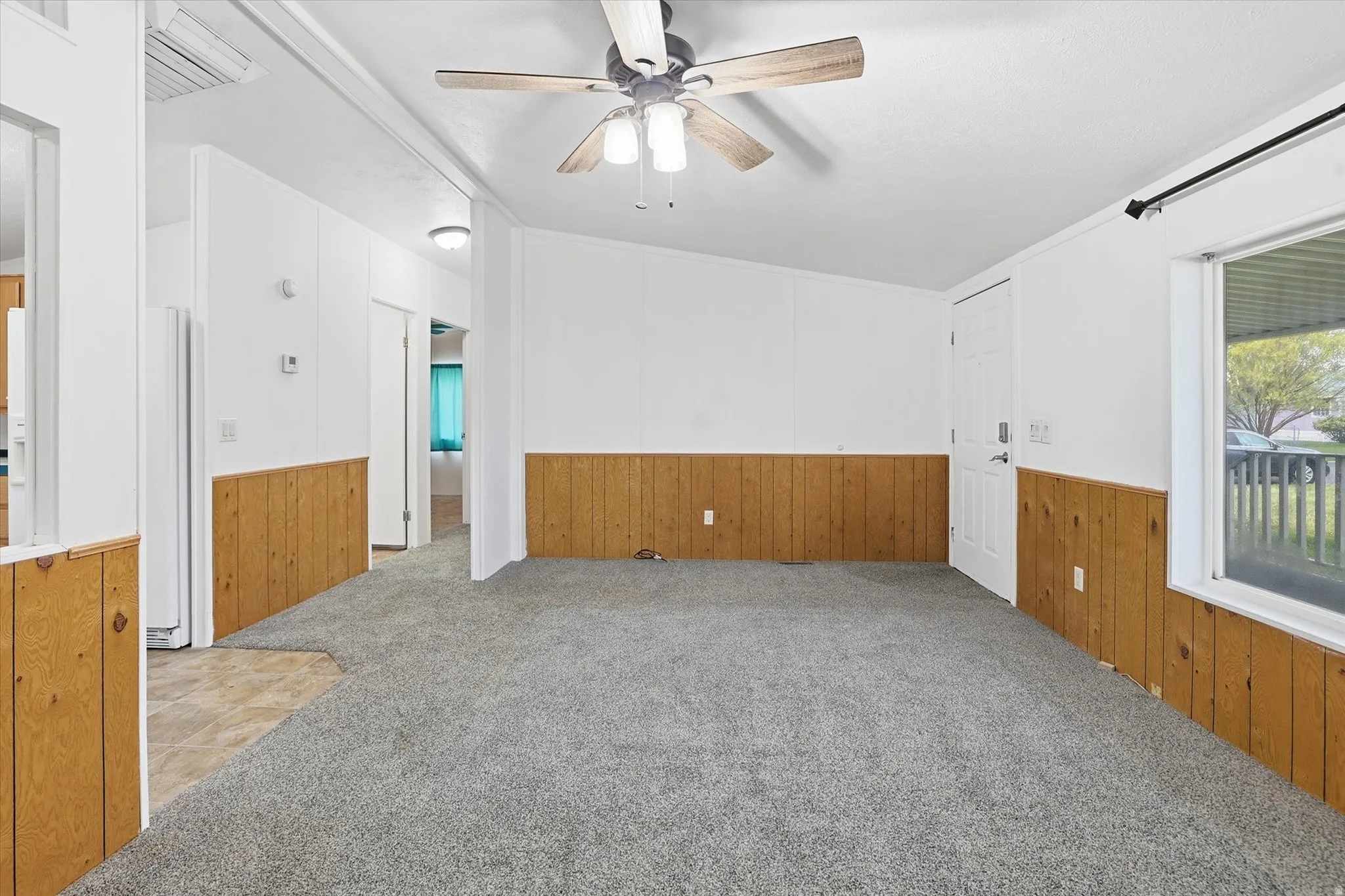Spare room featuring carpet flooring, wooden walls, a ceiling fan, and a wainscoted wall