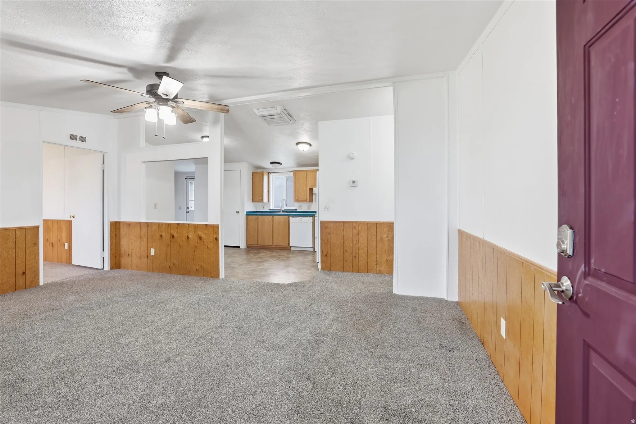 Unfurnished living room featuring light colored carpet, wooden walls, a wainscoted wall, and ceiling fan