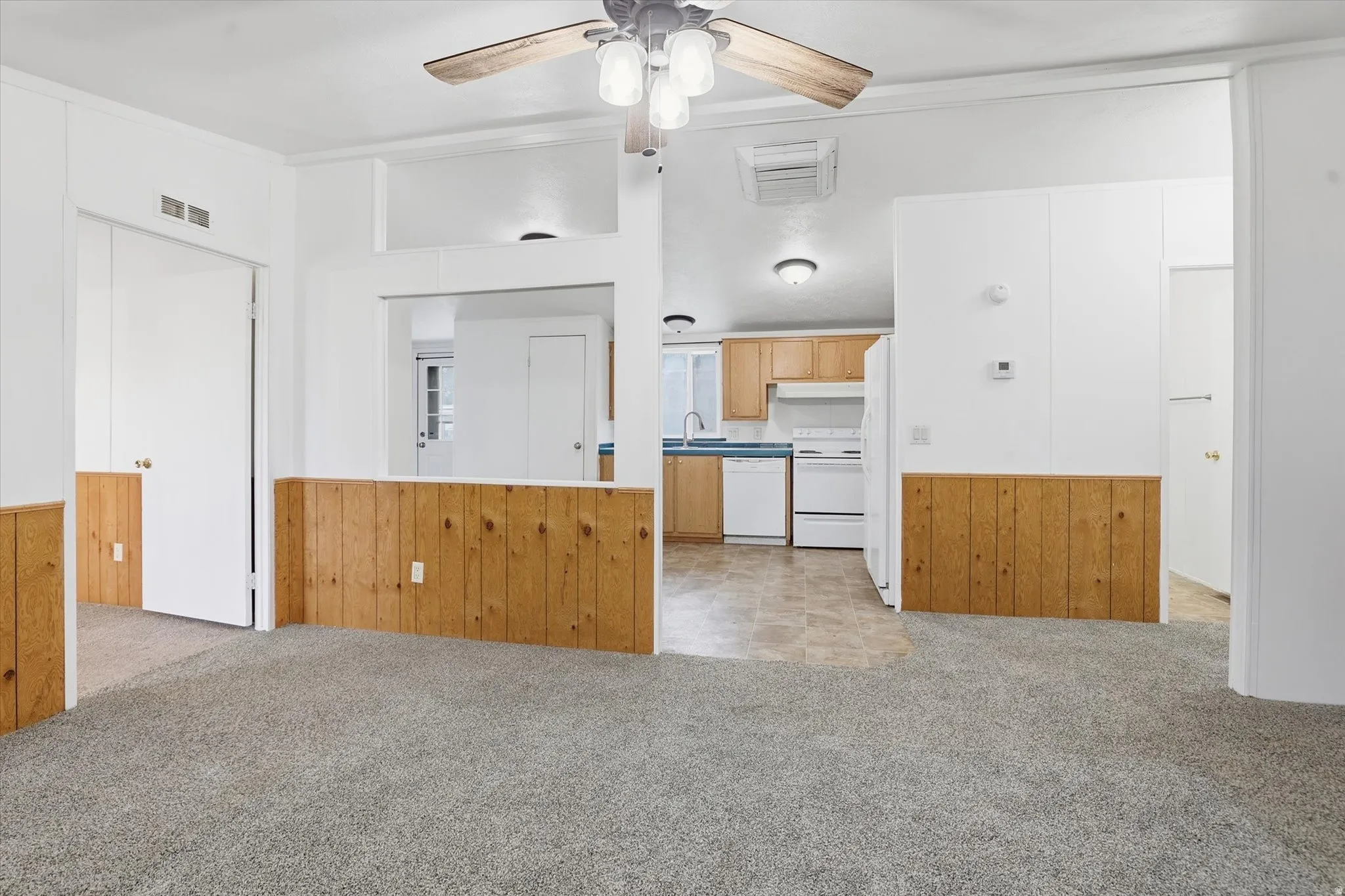 Kitchen with light colored carpet, wooden walls, ceiling fan, white appliances, and a wainscoted wall