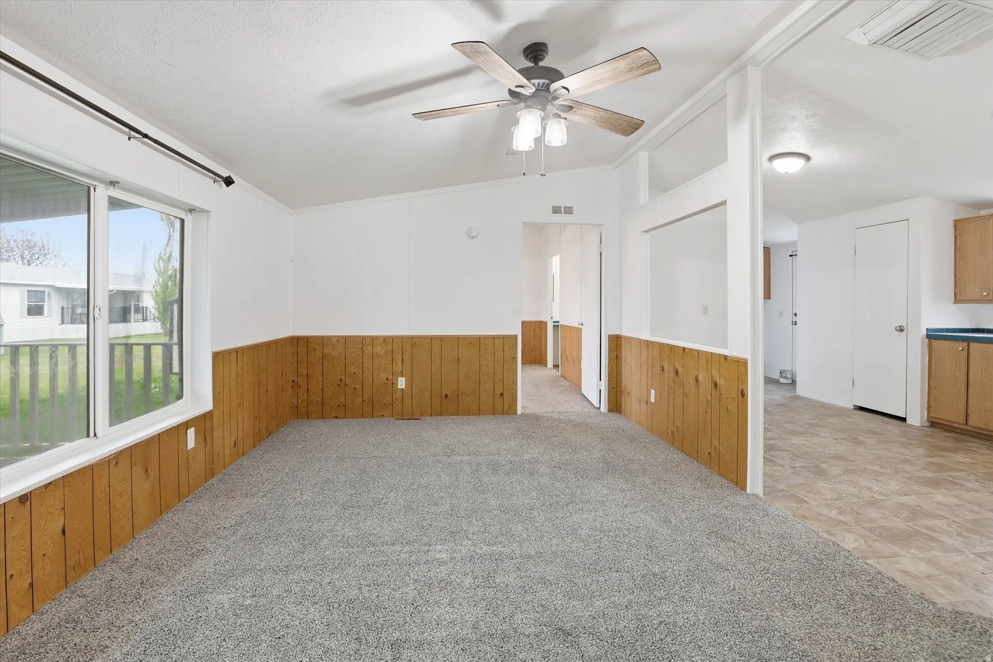 Unfurnished room featuring light carpet, wood walls, lofted ceiling, a ceiling fan, and wainscoting