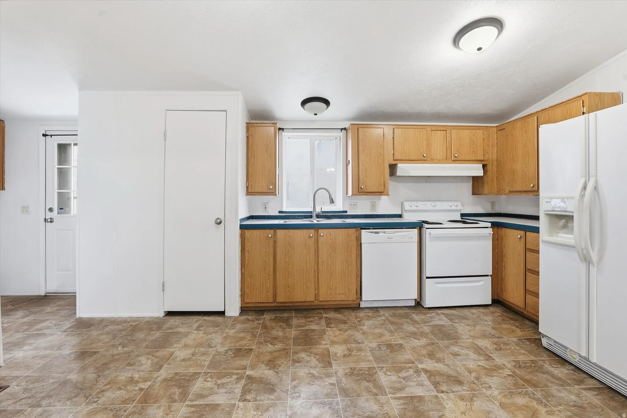Kitchen featuring white appliances, stone finish floors, wood finish cabinets, and dark countertops