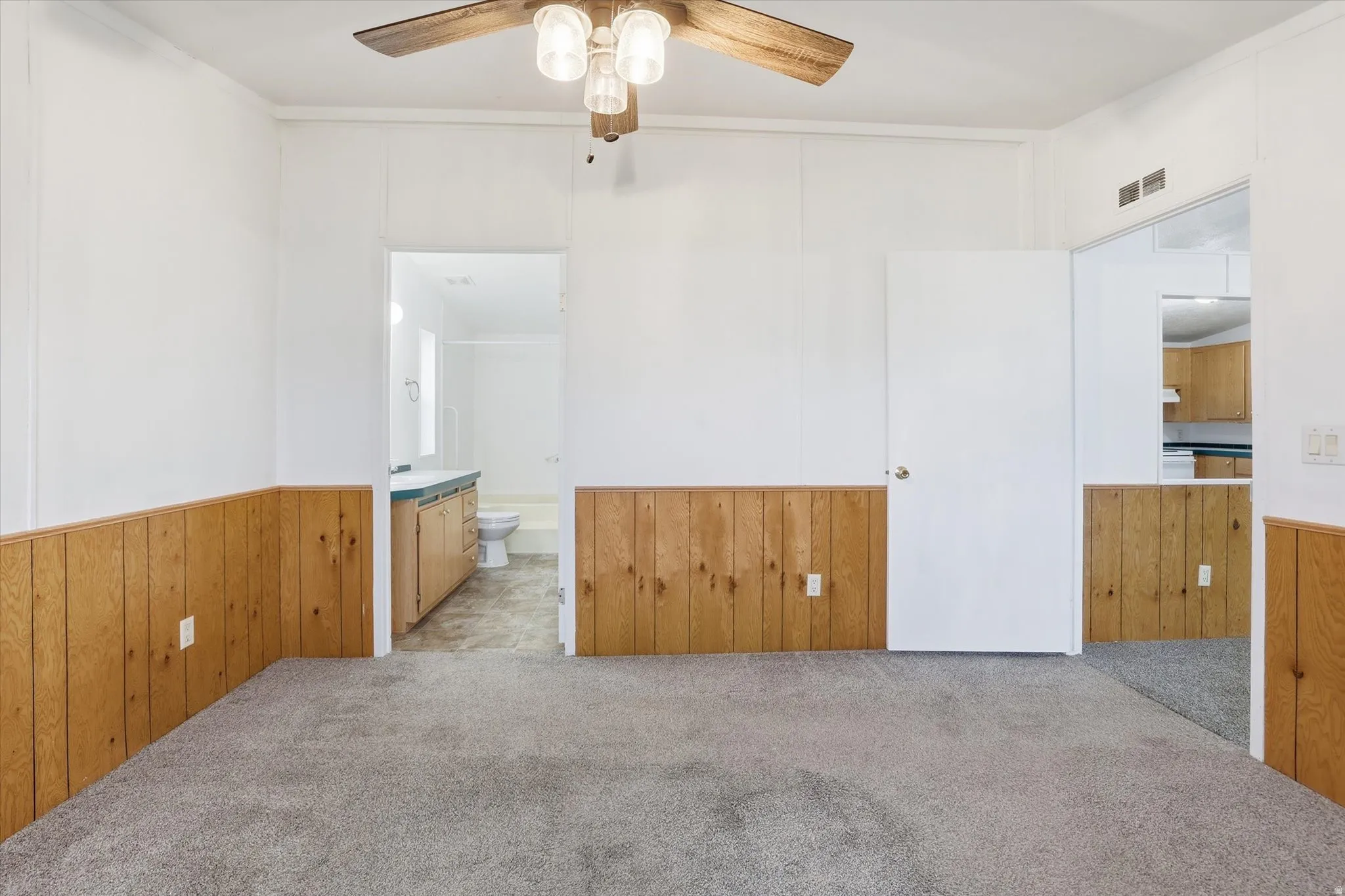 Carpeted empty room featuring wooden walls, a wainscoted wall, and a ceiling fan