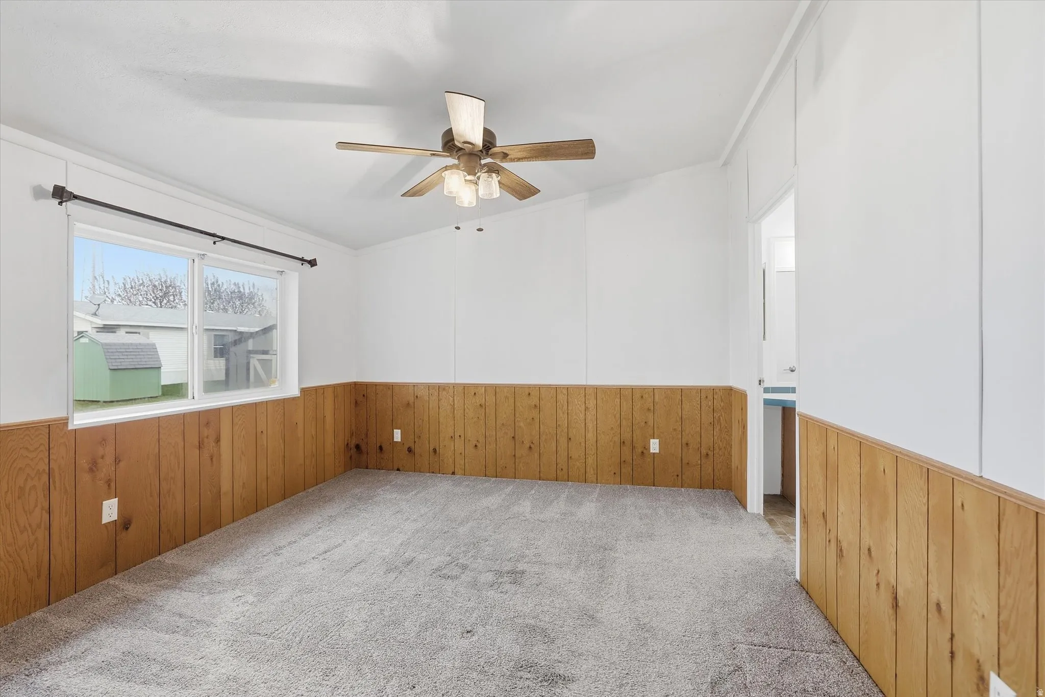 Empty room with wood walls, carpet flooring, a wainscoted wall, and a ceiling fan