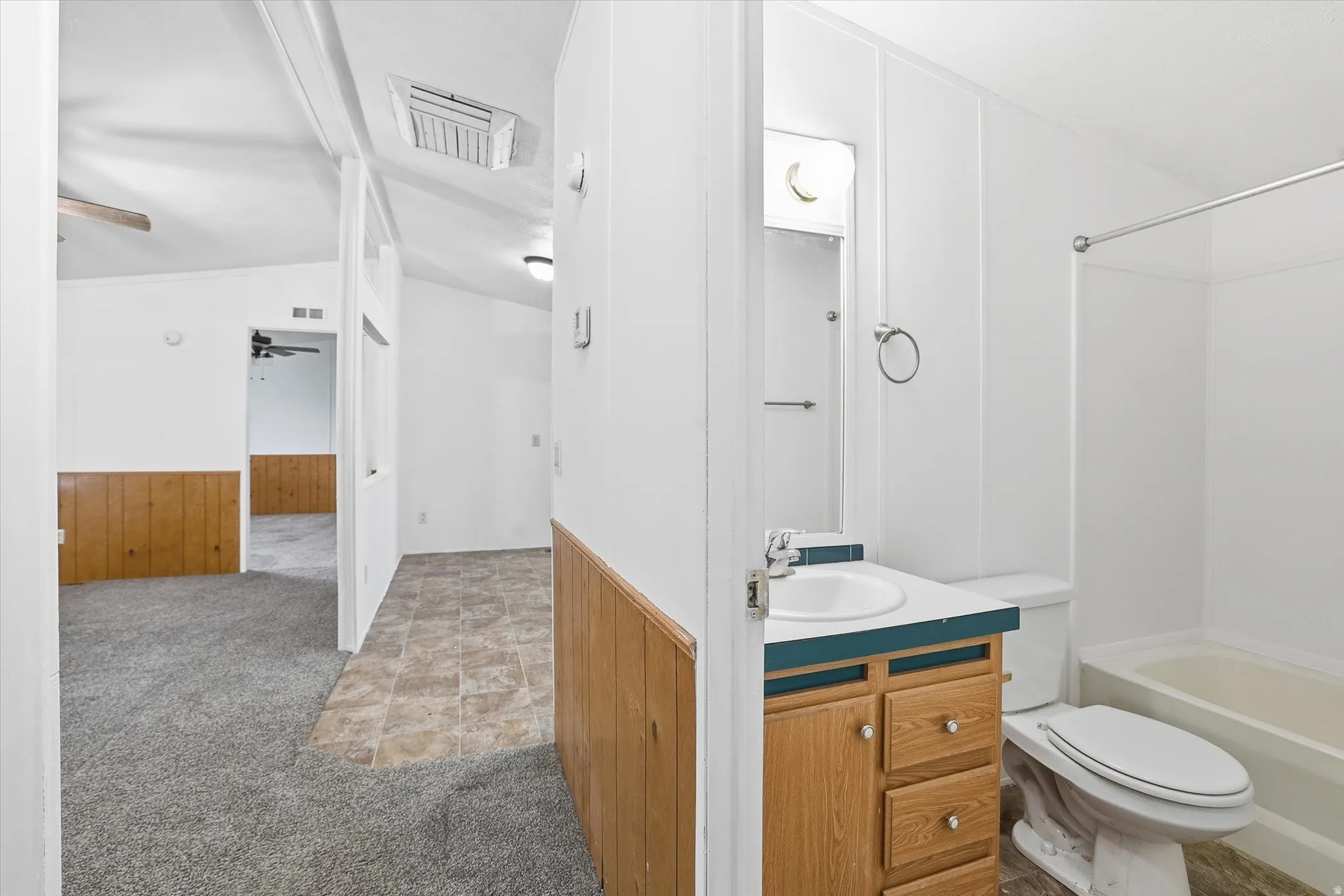 Bathroom with light carpet, wooden walls, lofted ceiling, vanity, and a wainscoted wall