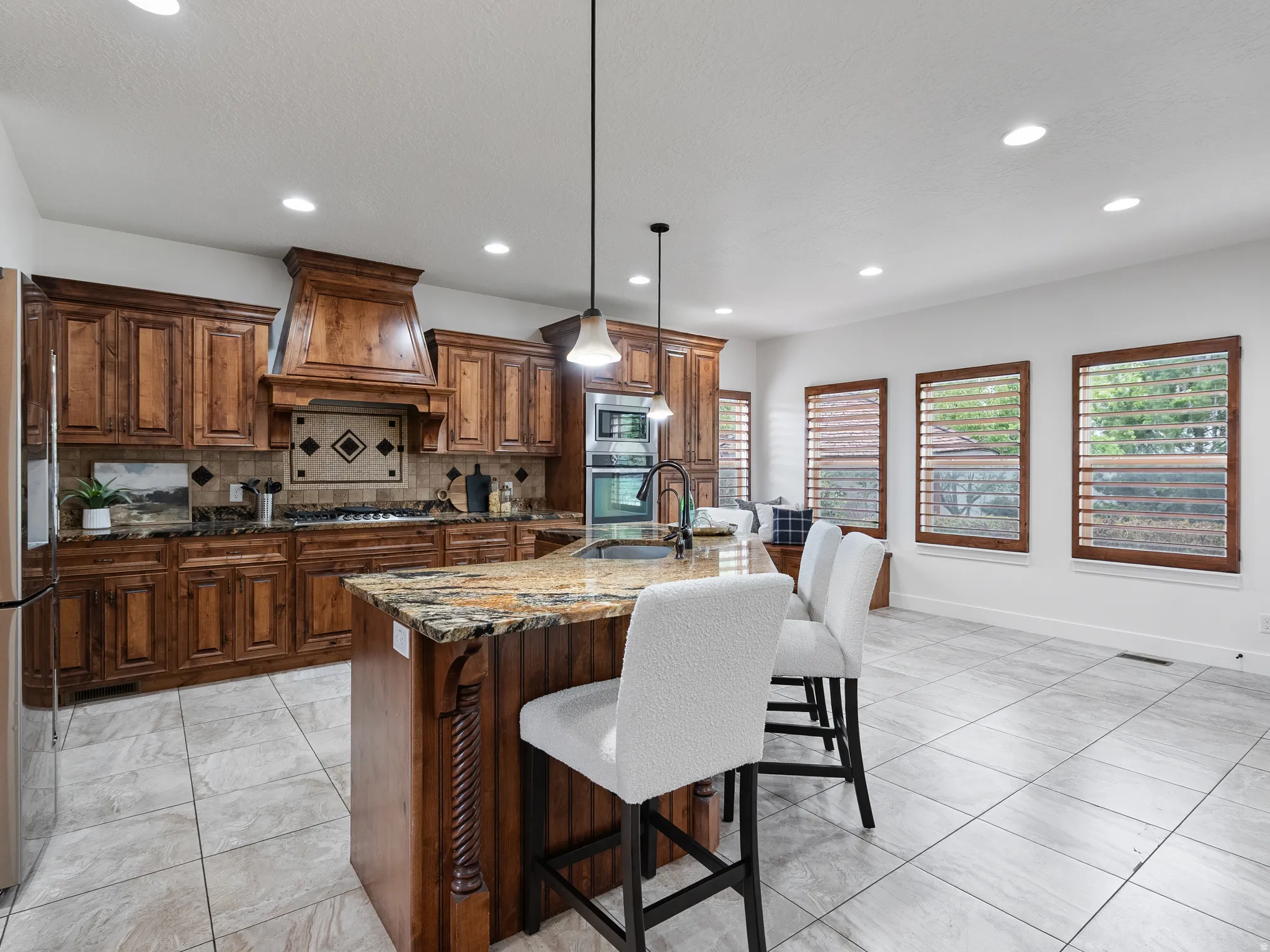 Kitchen with dark stone counters, a kitchen breakfast bar, pendant lighting, a center island with sink, and stainless steel appliances