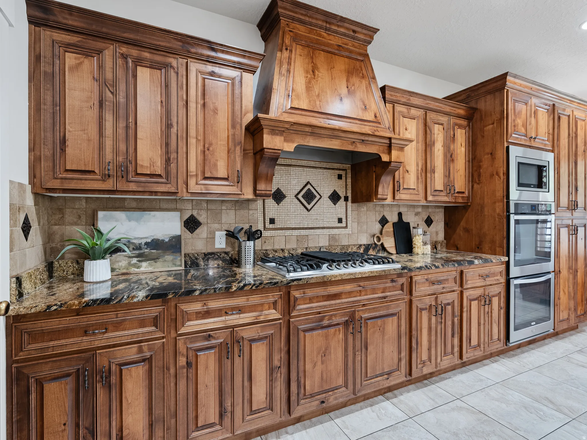 Kitchen with wood finish cabinets, dark stone counters, stainless steel appliances, tasteful backsplash, and light tile patterned floors