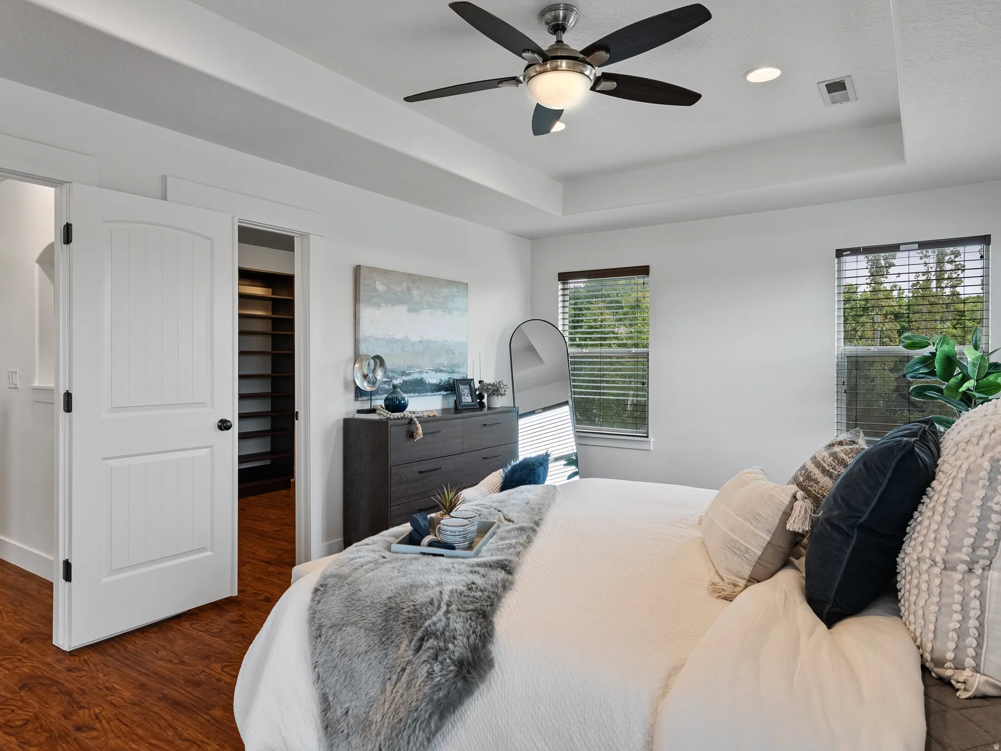 Bedroom with a raised ceiling, a walk in closet, dark wood-style flooring, ceiling fan, and recessed lighting
