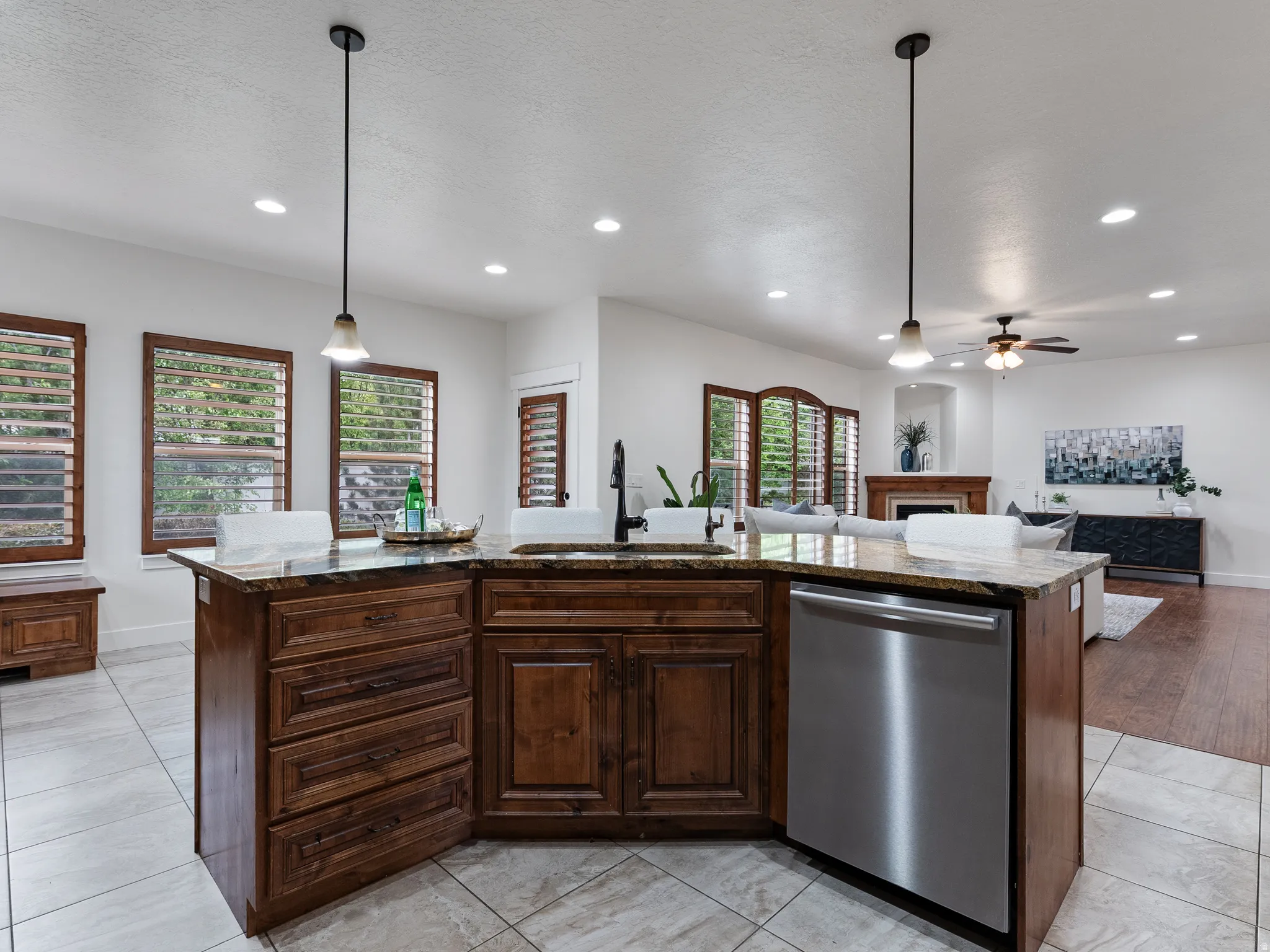 Kitchen with dark wood finish cabinetry, an island with sink, dishwasher, open floor plan, and light tile patterned flooring