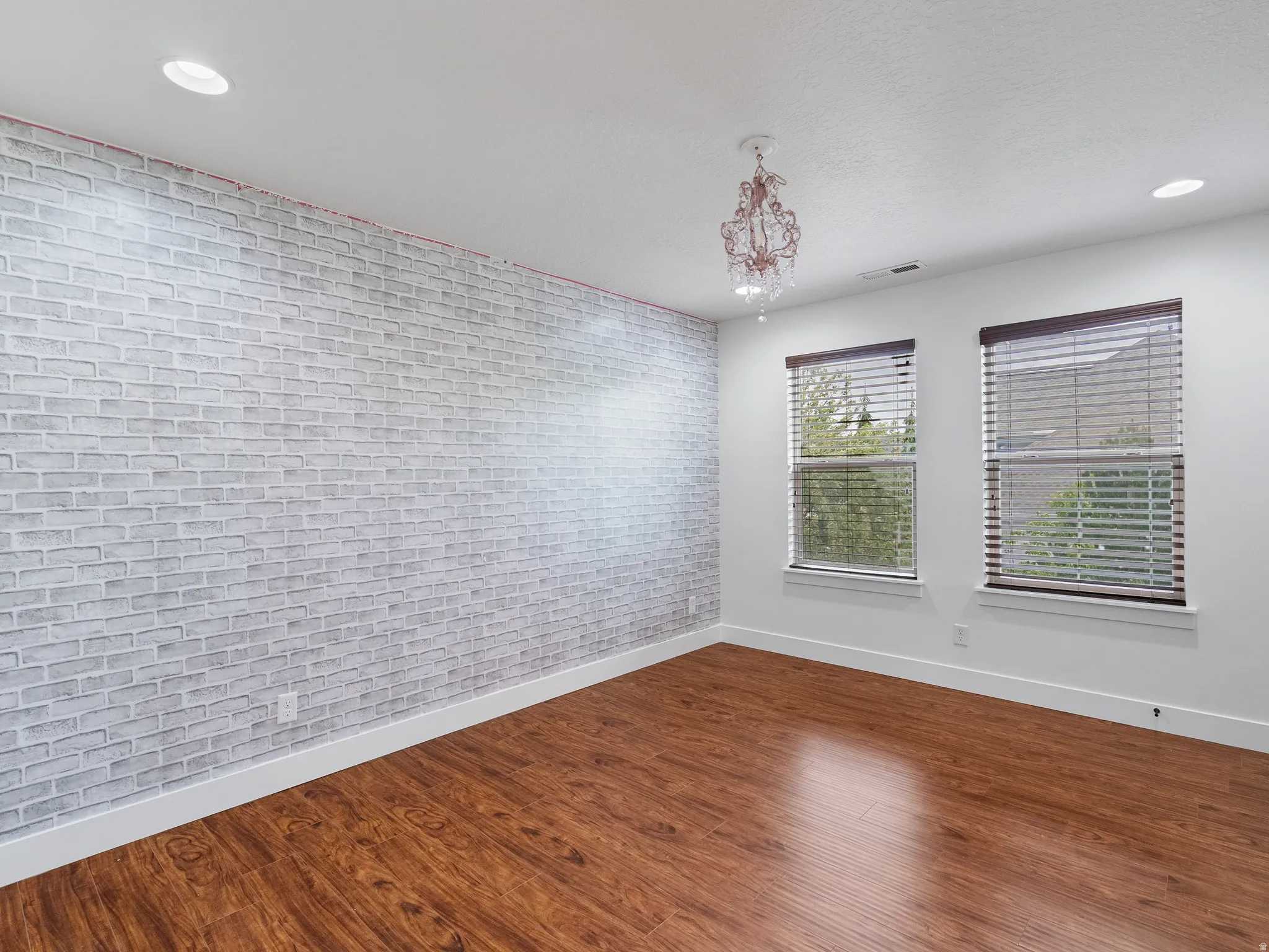Empty room featuring brick wall, dark wood-style floors, and a chandelier