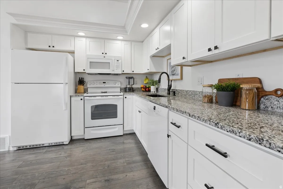 Kitchen with white appliances, recessed lighting, white cabinets, light stone countertops, and dark wood-type flooring
