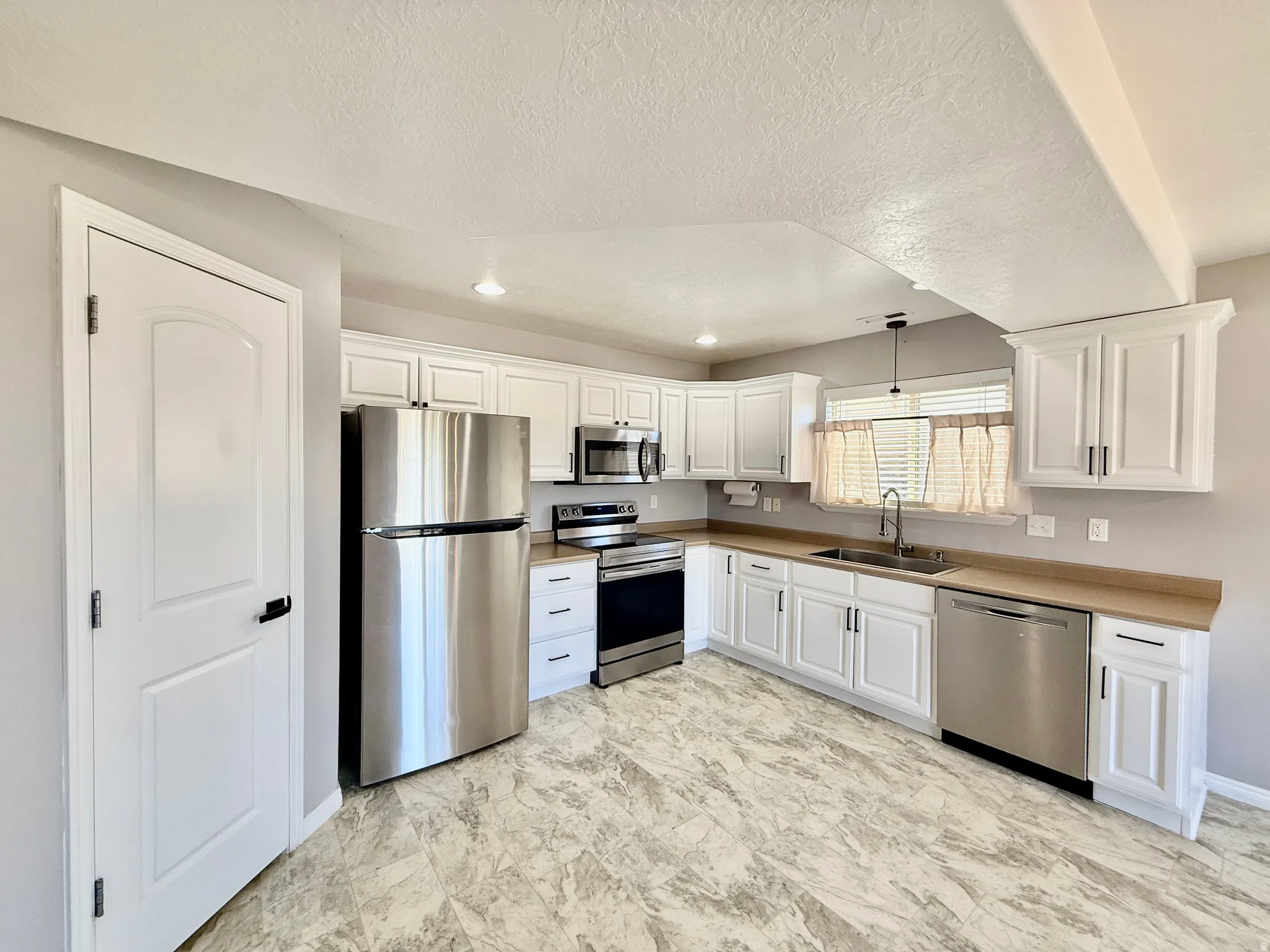 Kitchen featuring stainless steel appliances, white cabinetry, light countertops, and patterned flooring