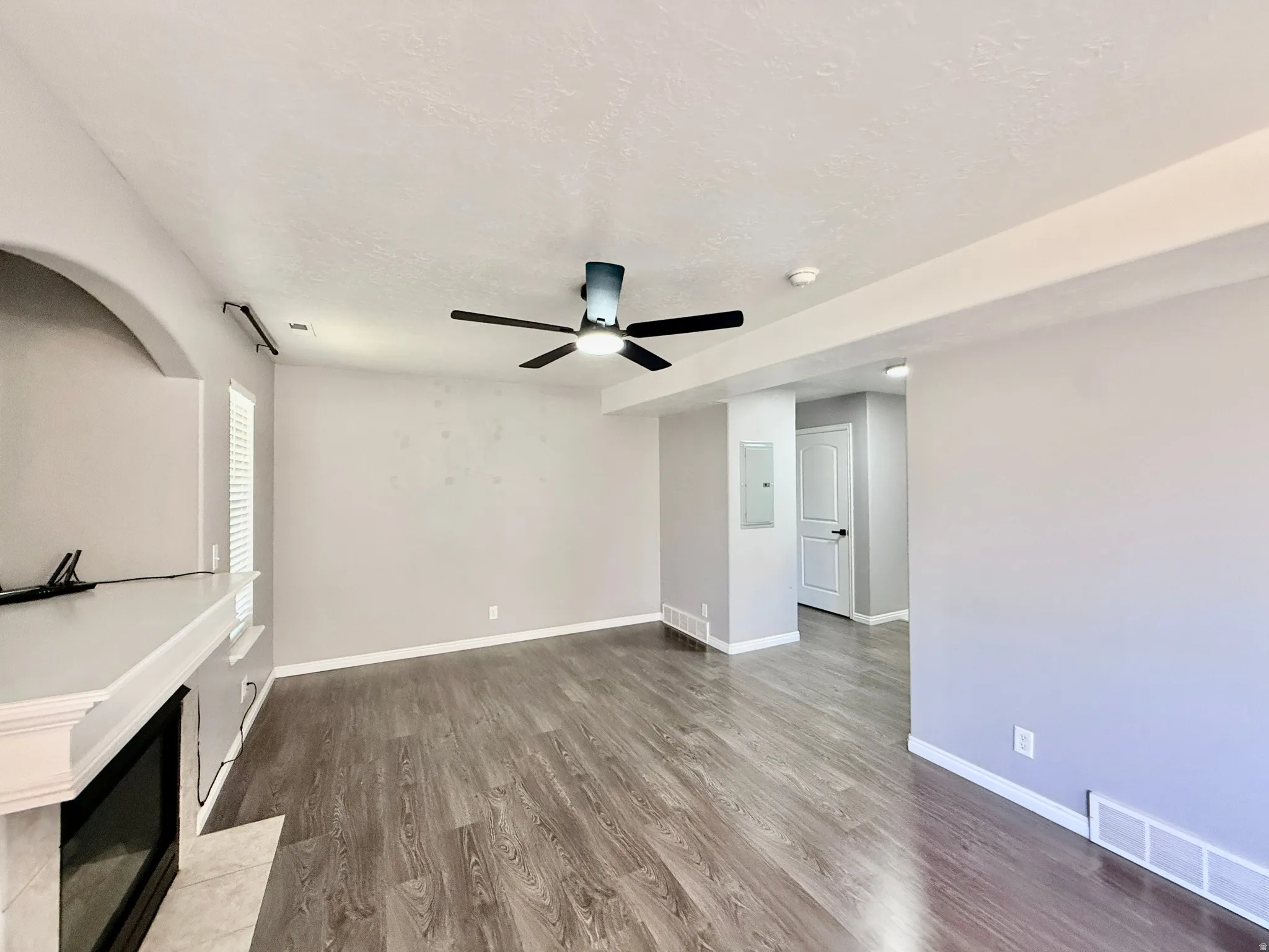 Spacious living area featuring wood-finish flooring, a ceiling fan, and light gray wall tones