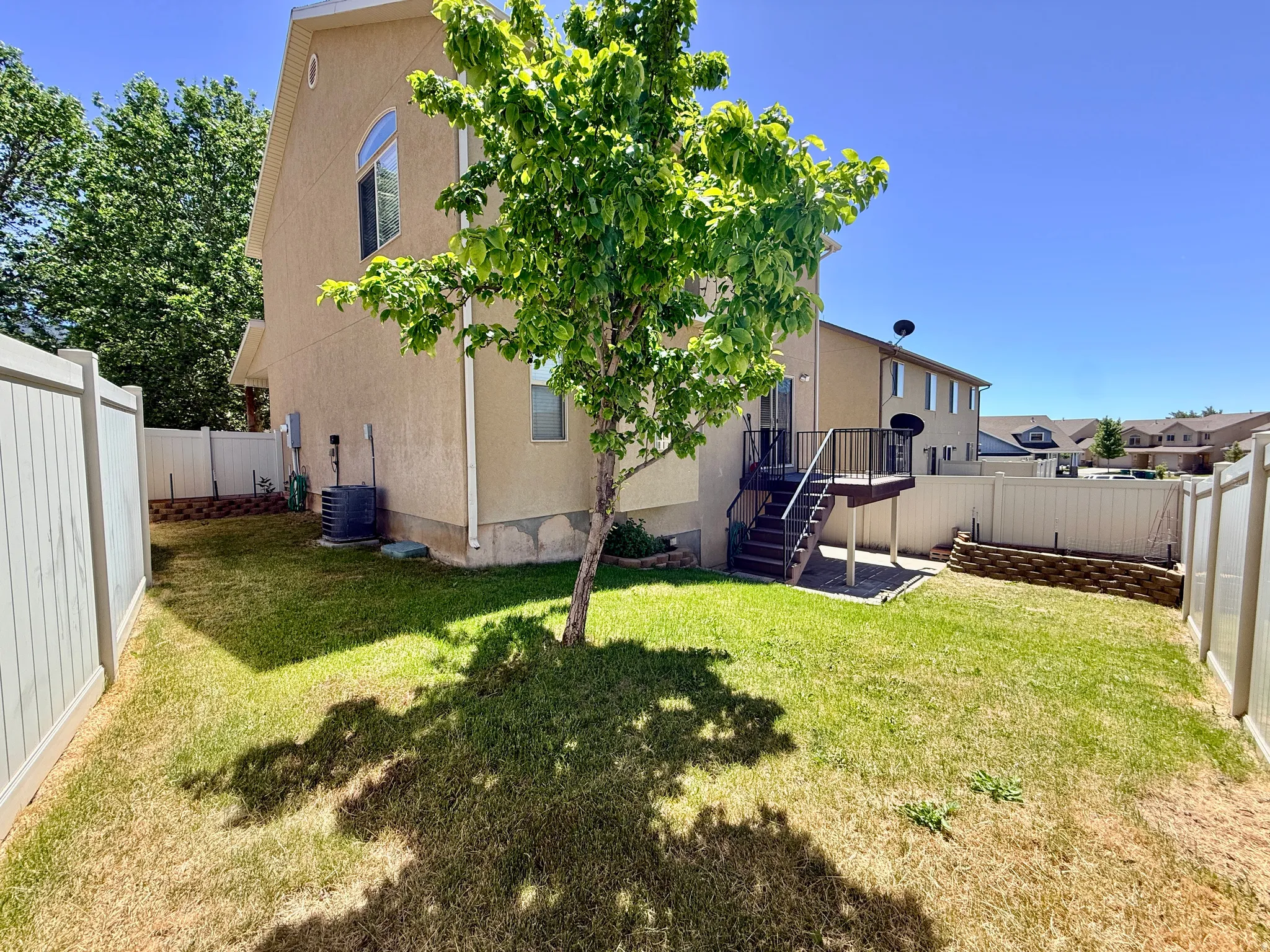 Expansive fenced backyard featuring a wood deck with stairs, a mature tree, and a terraced garden bed