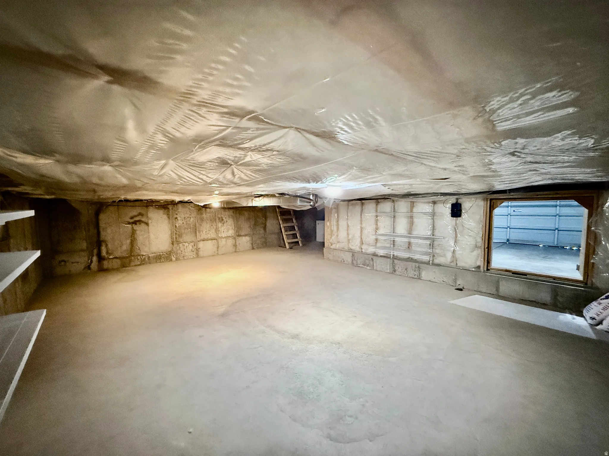 Spacious basement area featuring a concrete floor, exposed concrete foundation walls, and a large opening to what appears to be a garage