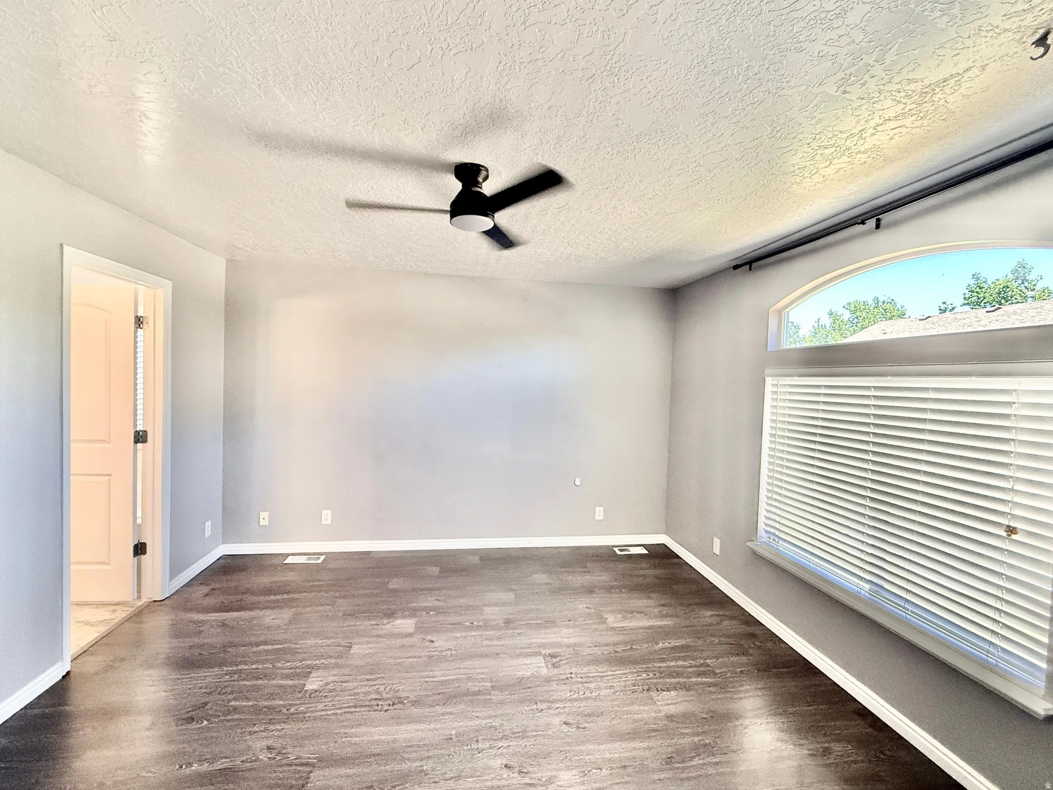 Spacious room featuring wood-finish flooring, light gray wall tones, and white baseboards