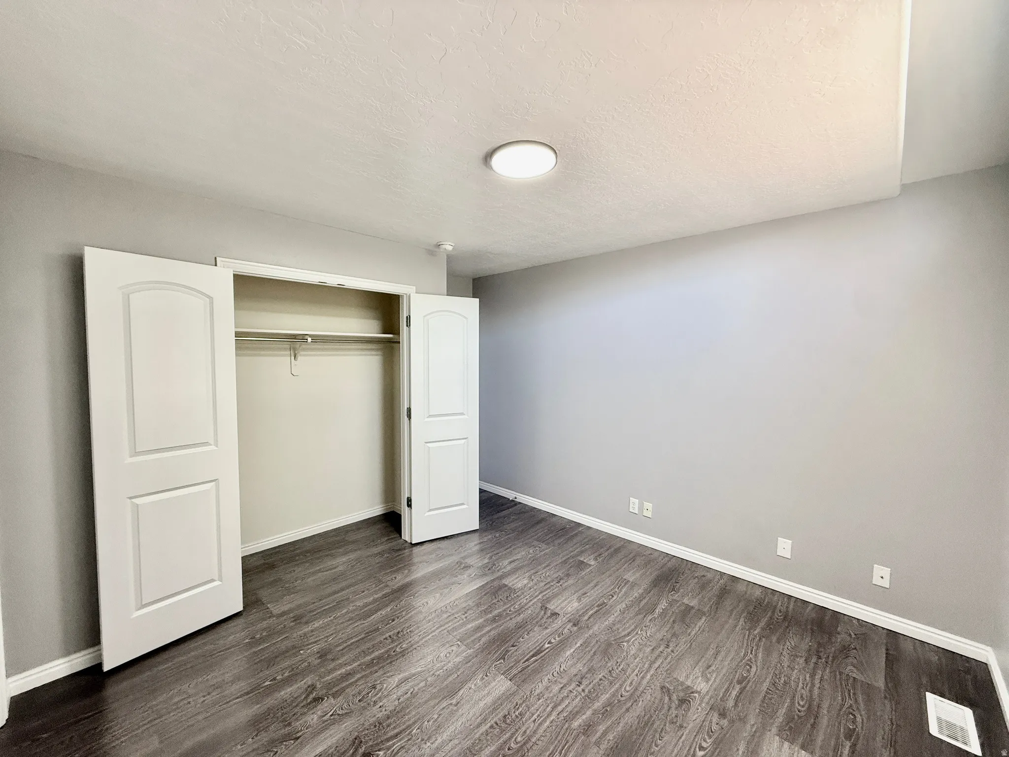 Spacious room featuring wood-finish flooring, light gray wall tones, and white baseboards