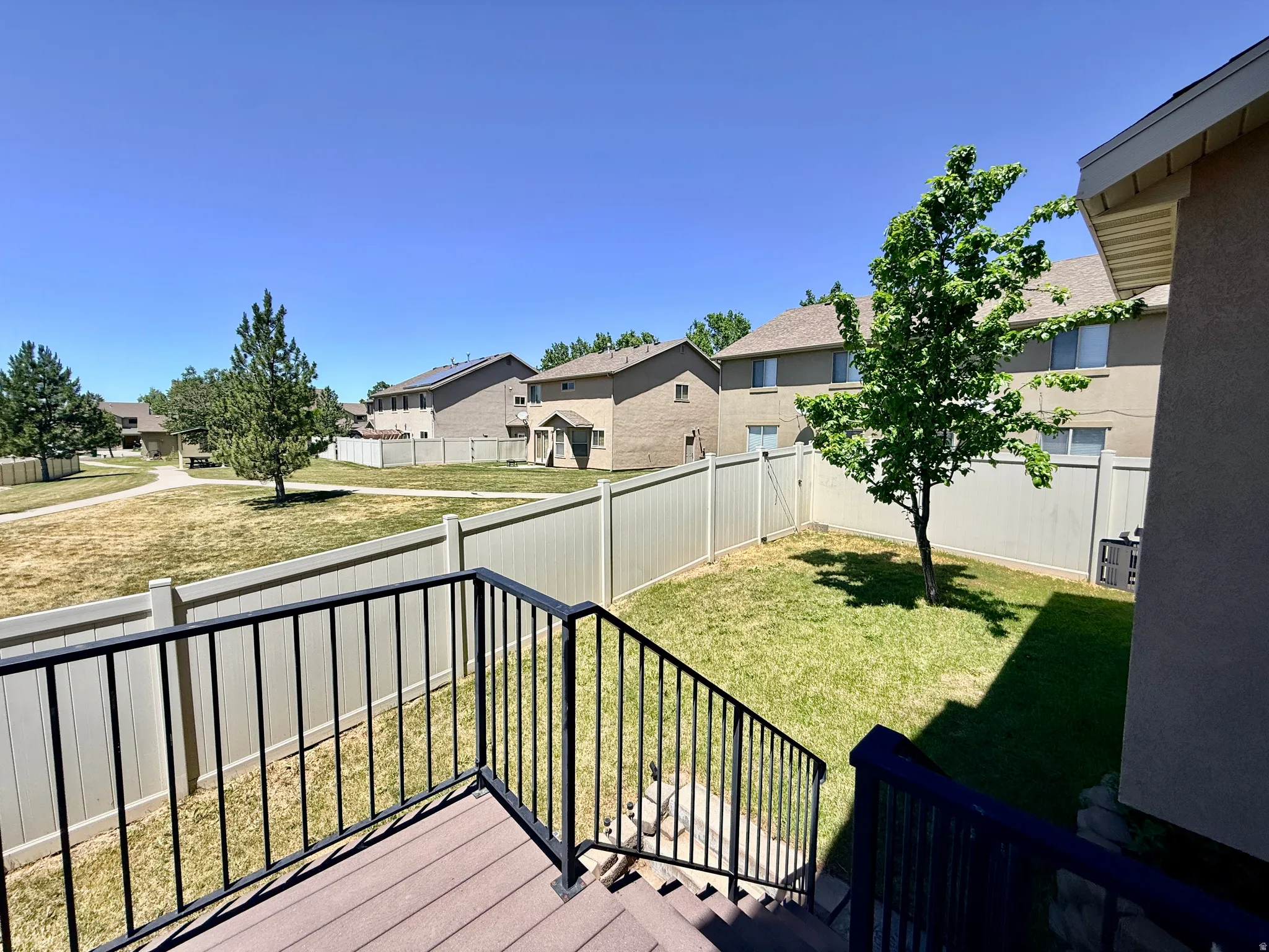 Wood-finish deck with black metal railings overlooking a private fenced yard with a mature tree