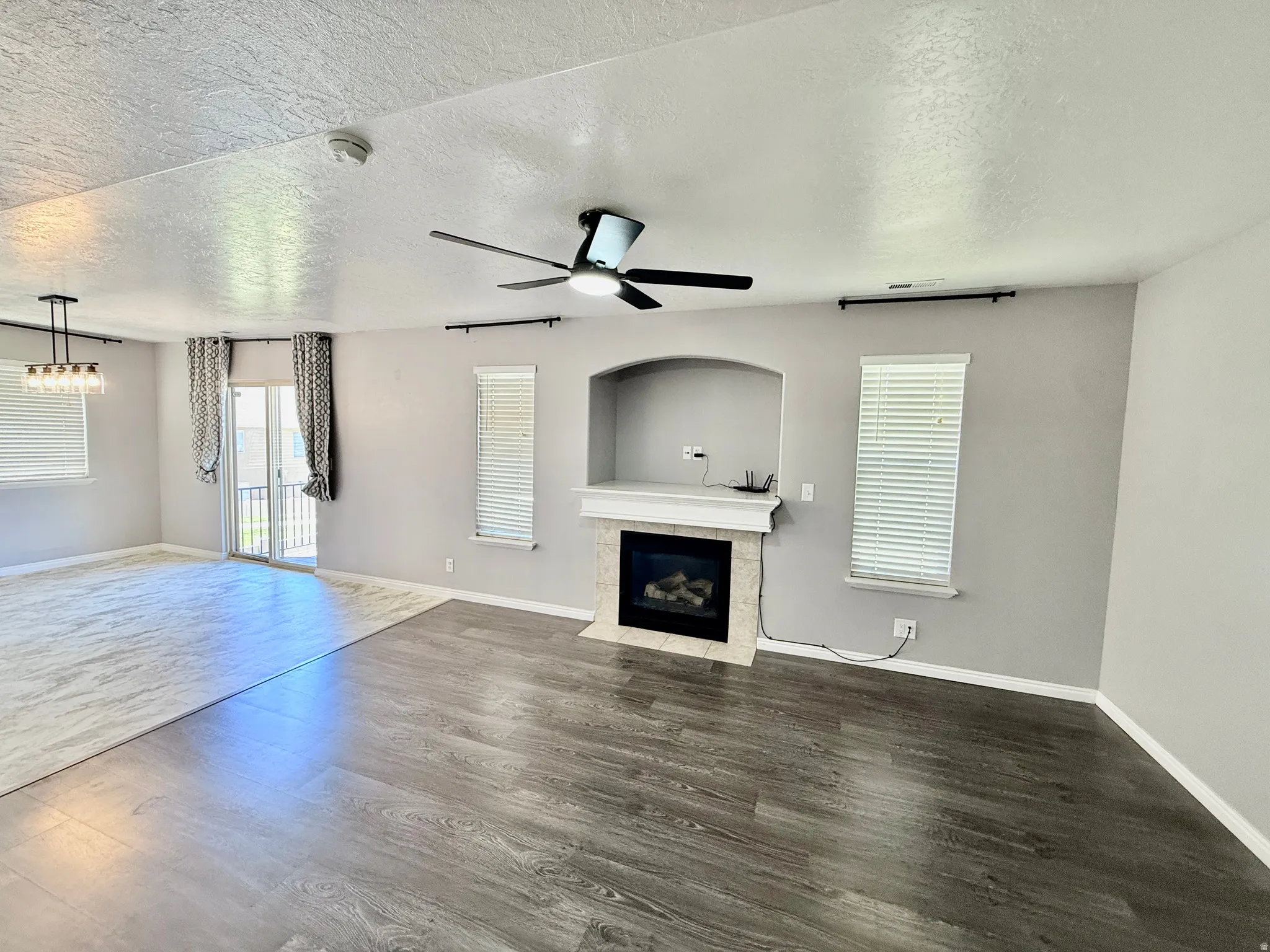 Living area featuring wood-finish flooring, a fireplace with a stone surround and mantle, a ceiling fan, and multiple windows with blinds