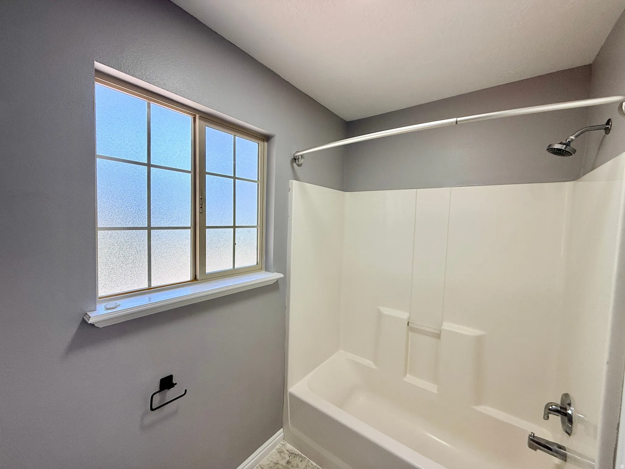 Bathroom featuring a full-size tub with an integrated shower, chrome fixtures, and a privacy-glass window