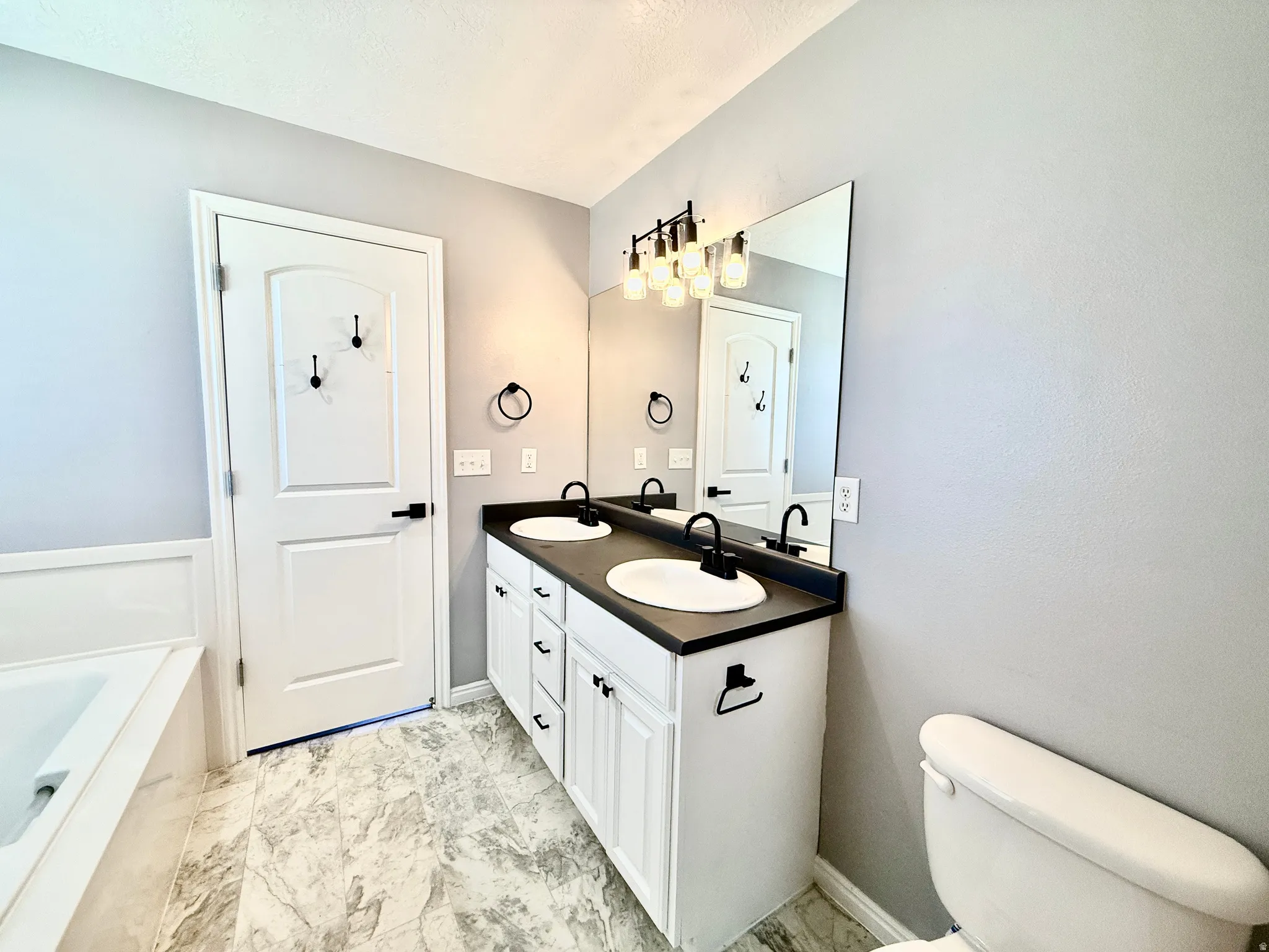Vanity featuring dual white undermount sinks with matte black faucets, a dark countertop, and white cabinet storage