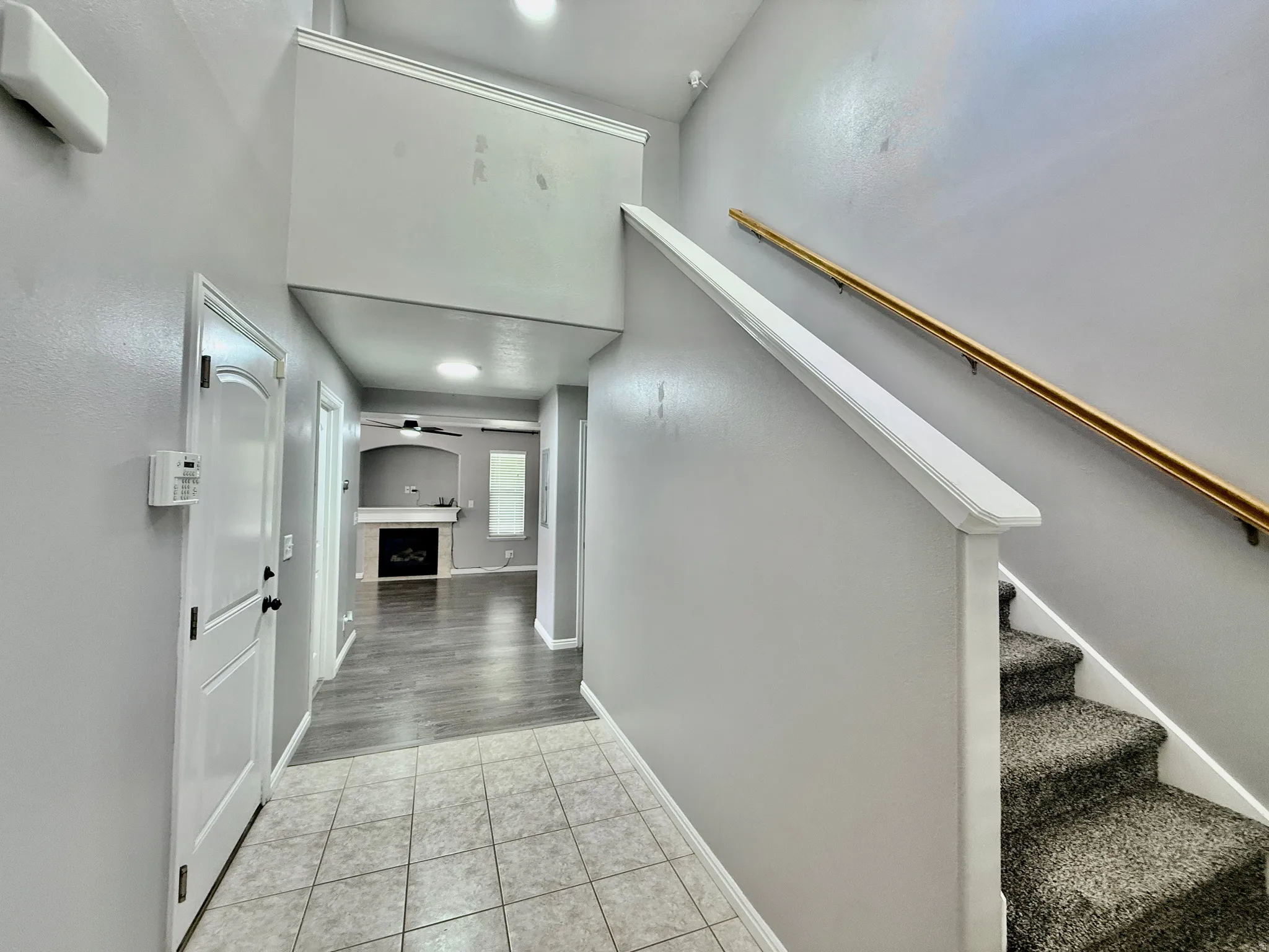Entryway featuring a tiled floor, carpeted staircase with a brass handrail, and a white paneled door