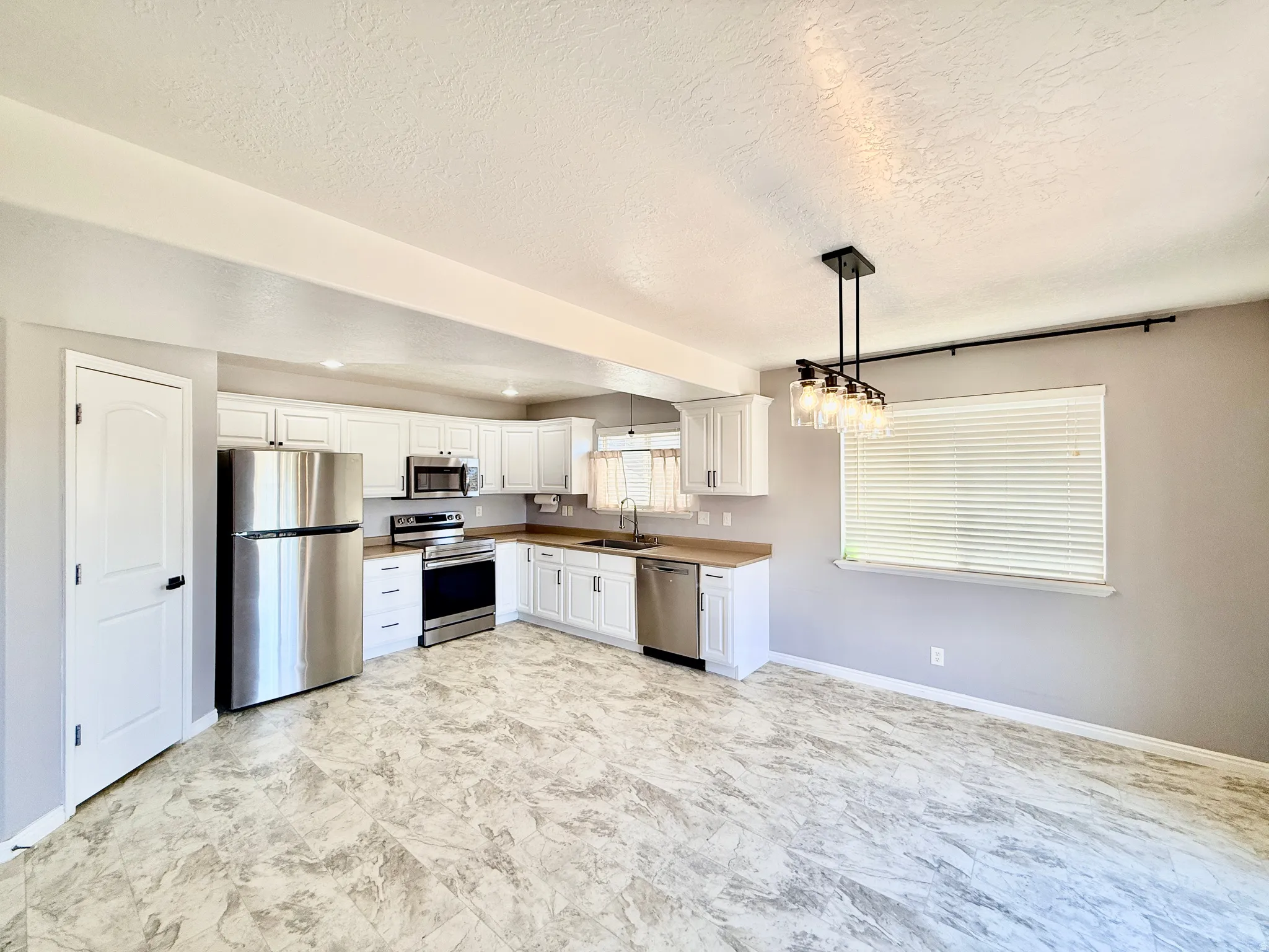 Kitchen area featuring white cabinetry, stainless steel appliances, light wood-finish countertops, and patterned floor tiling