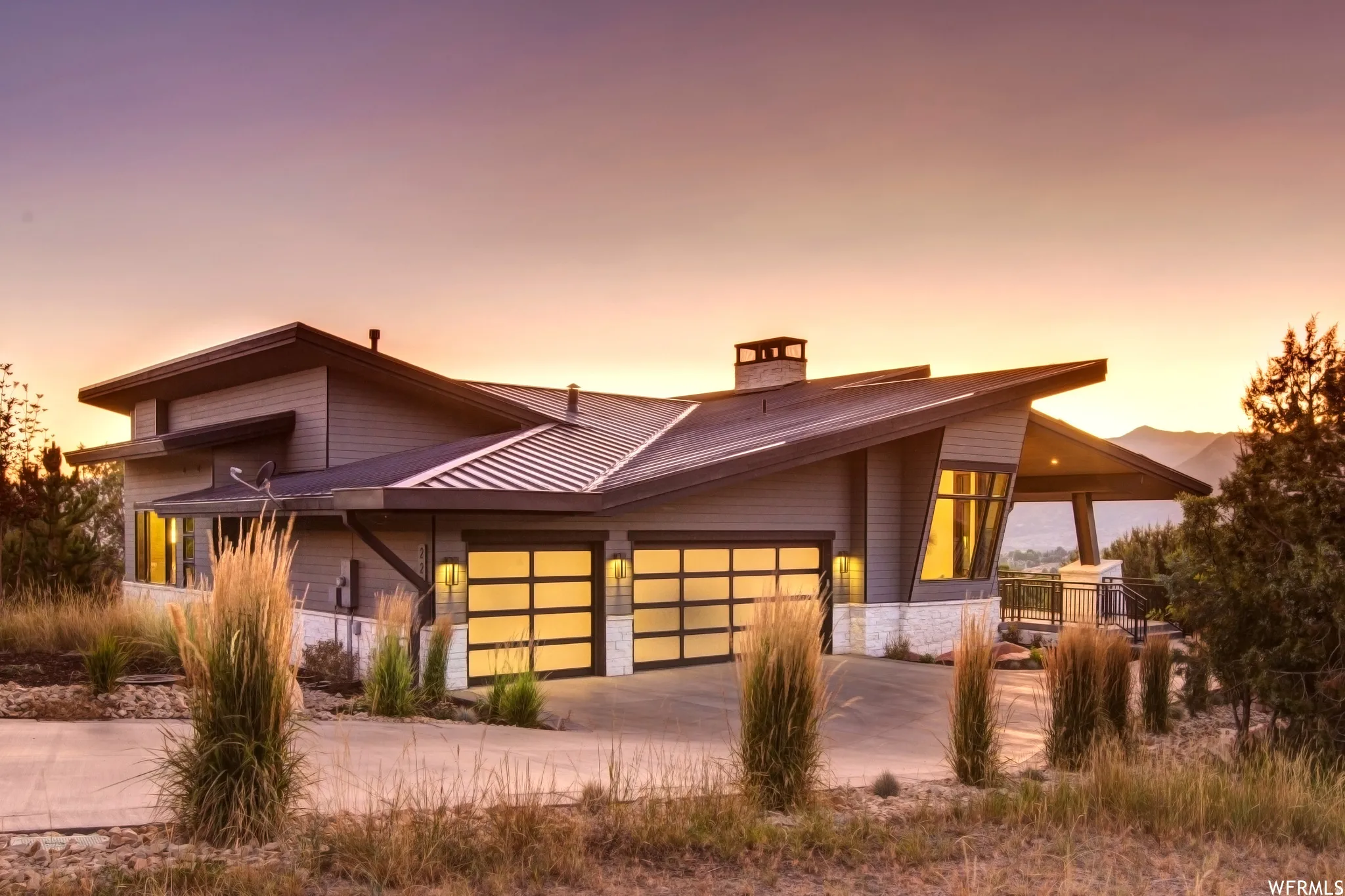 View of front of property featuring a garage, driveway, a chimney, a porch, and a standing seam roof