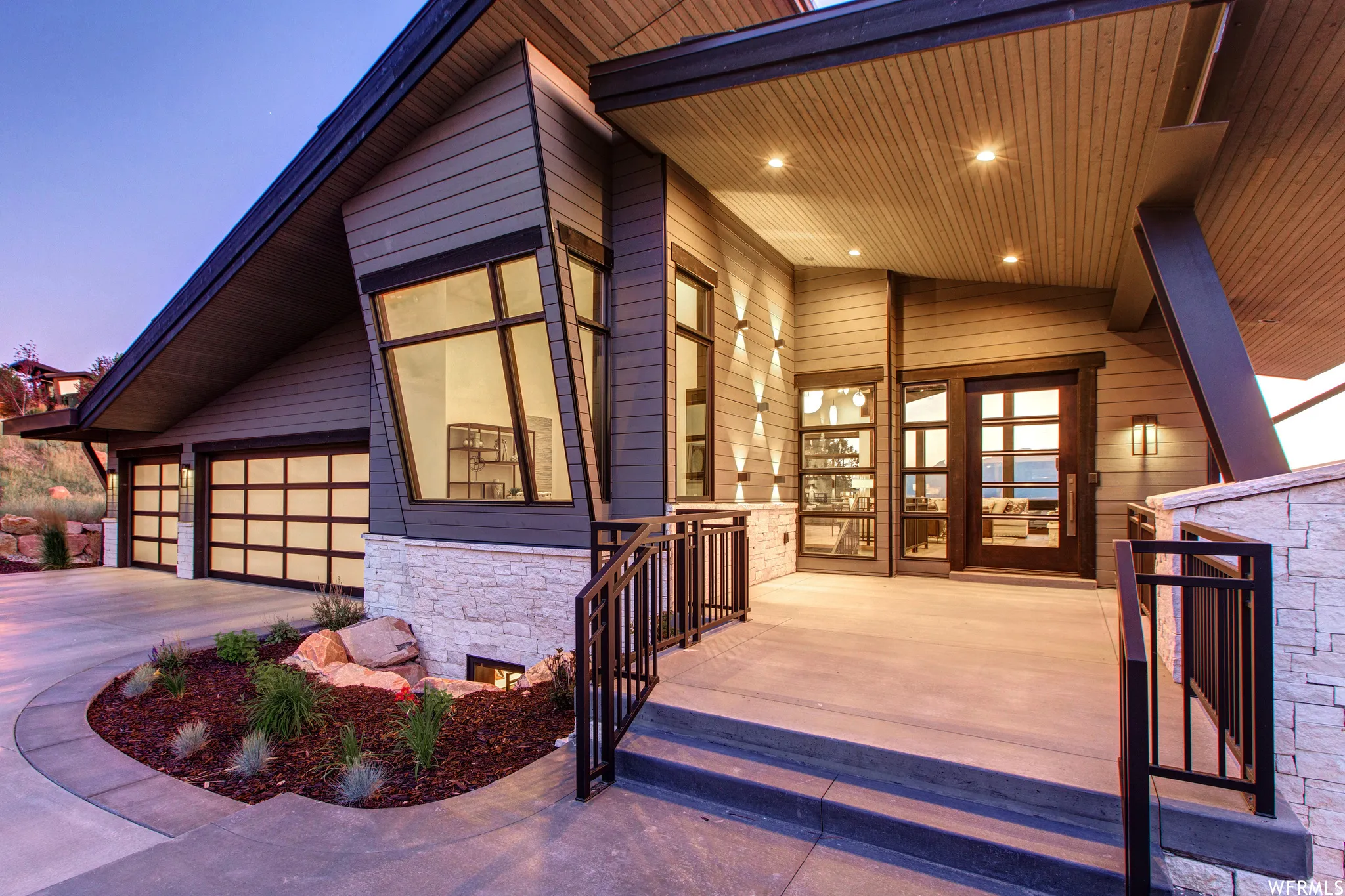 Property entrance featuring stone siding, driveway, covered porch, and a garage