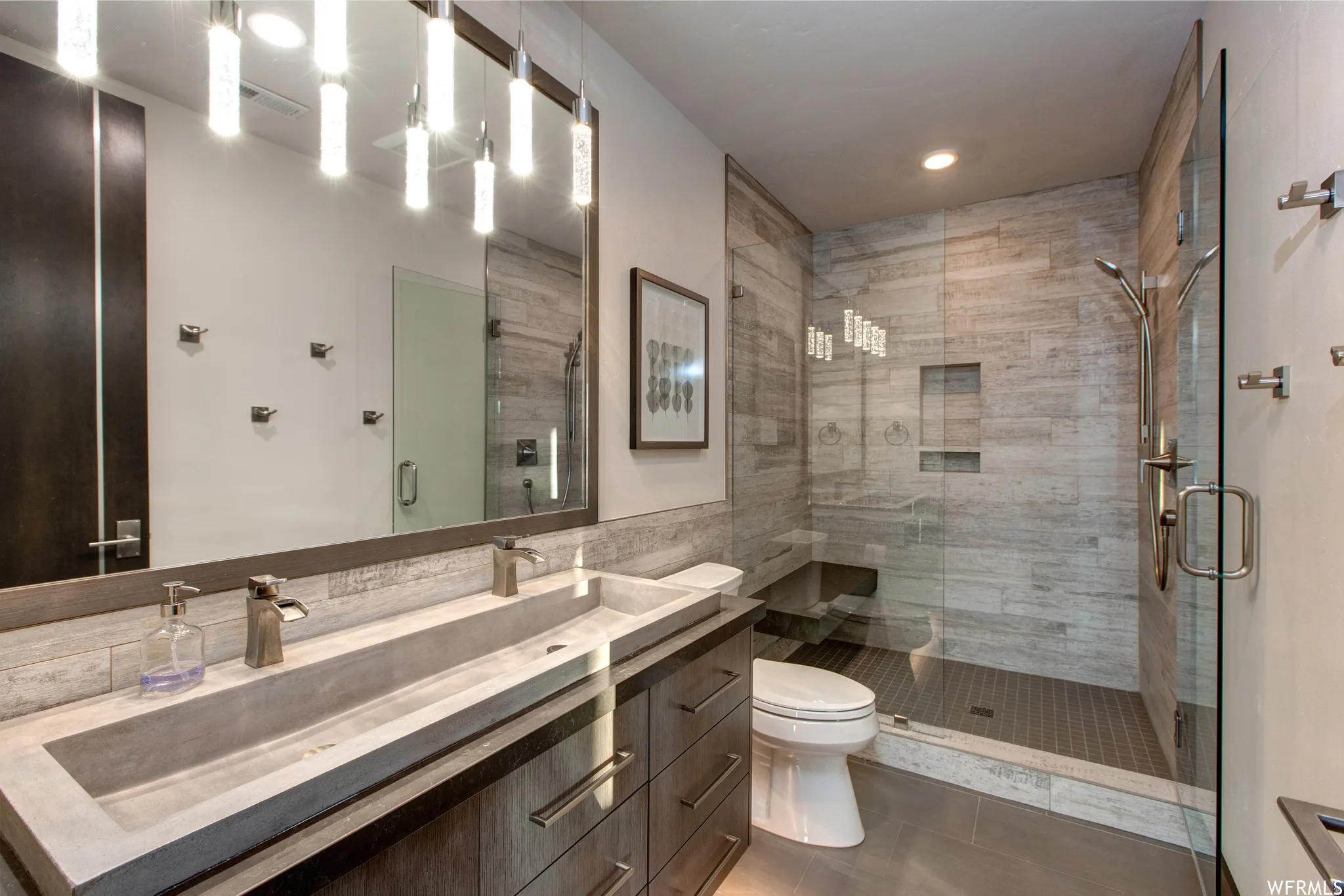 Bathroom with double vanity, a shower stall, tile walls, and recessed lighting