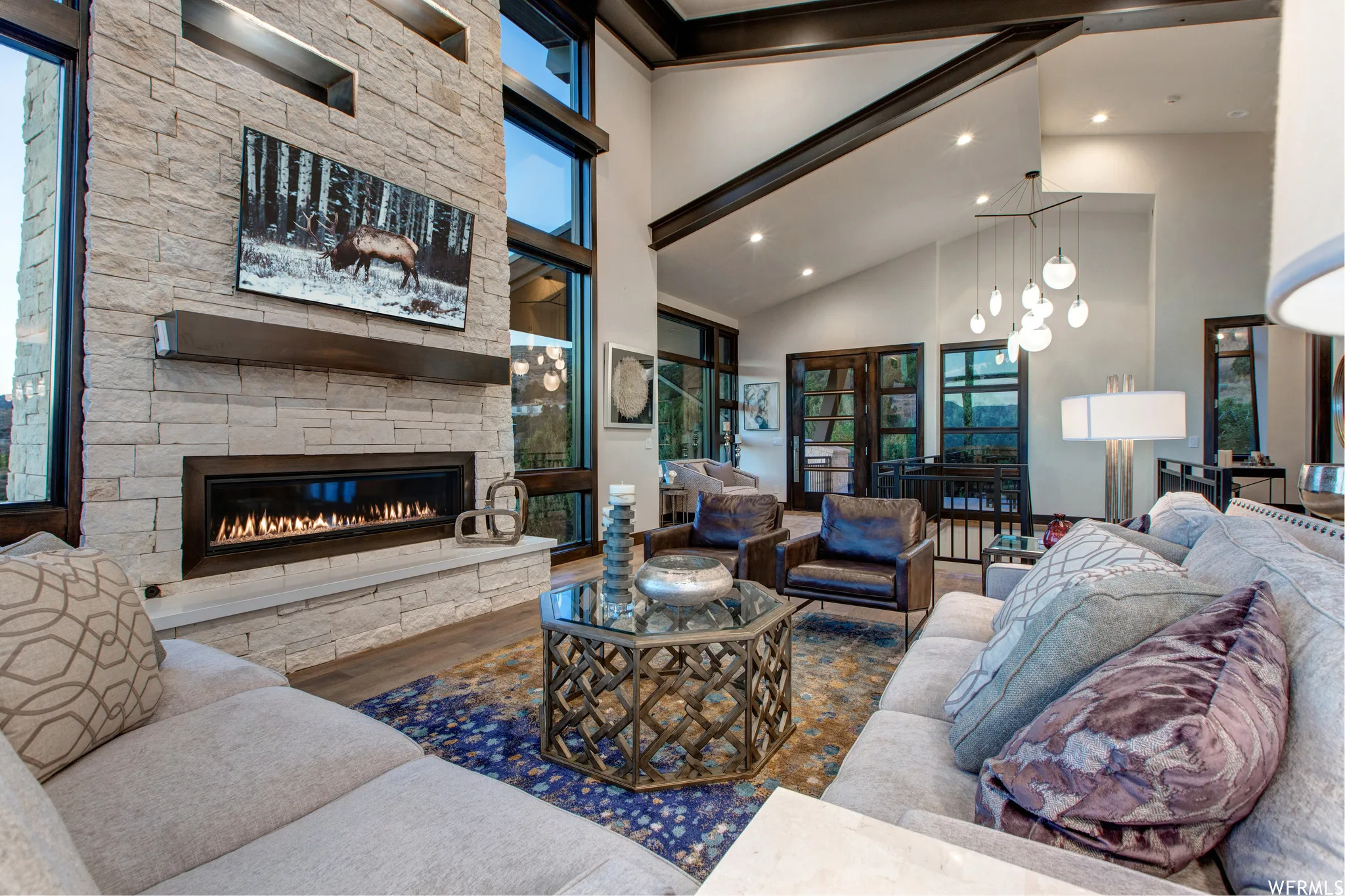 Living room featuring wood finished floors, a stone fireplace, lofted ceiling, and hanging lights