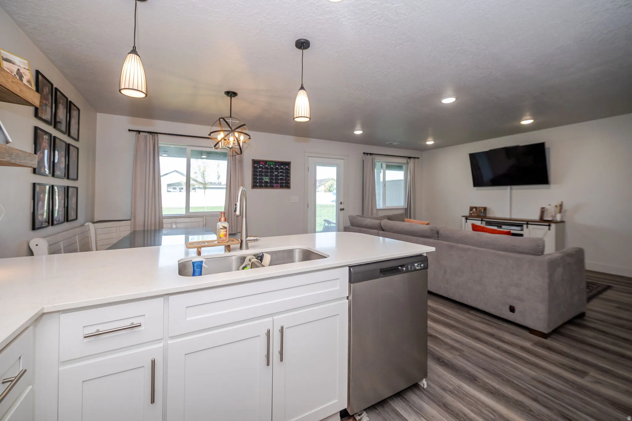 Kitchen with white cabinetry, open floor plan, dishwasher, a chandelier, and light stone counters