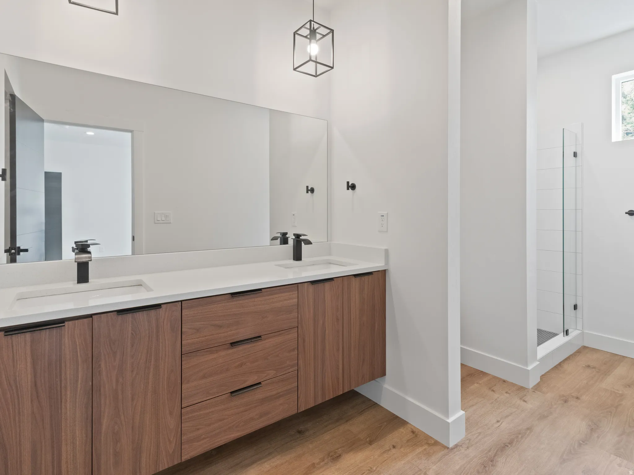 Full bath with double vanity, a tile shower, and light wood-style floors
