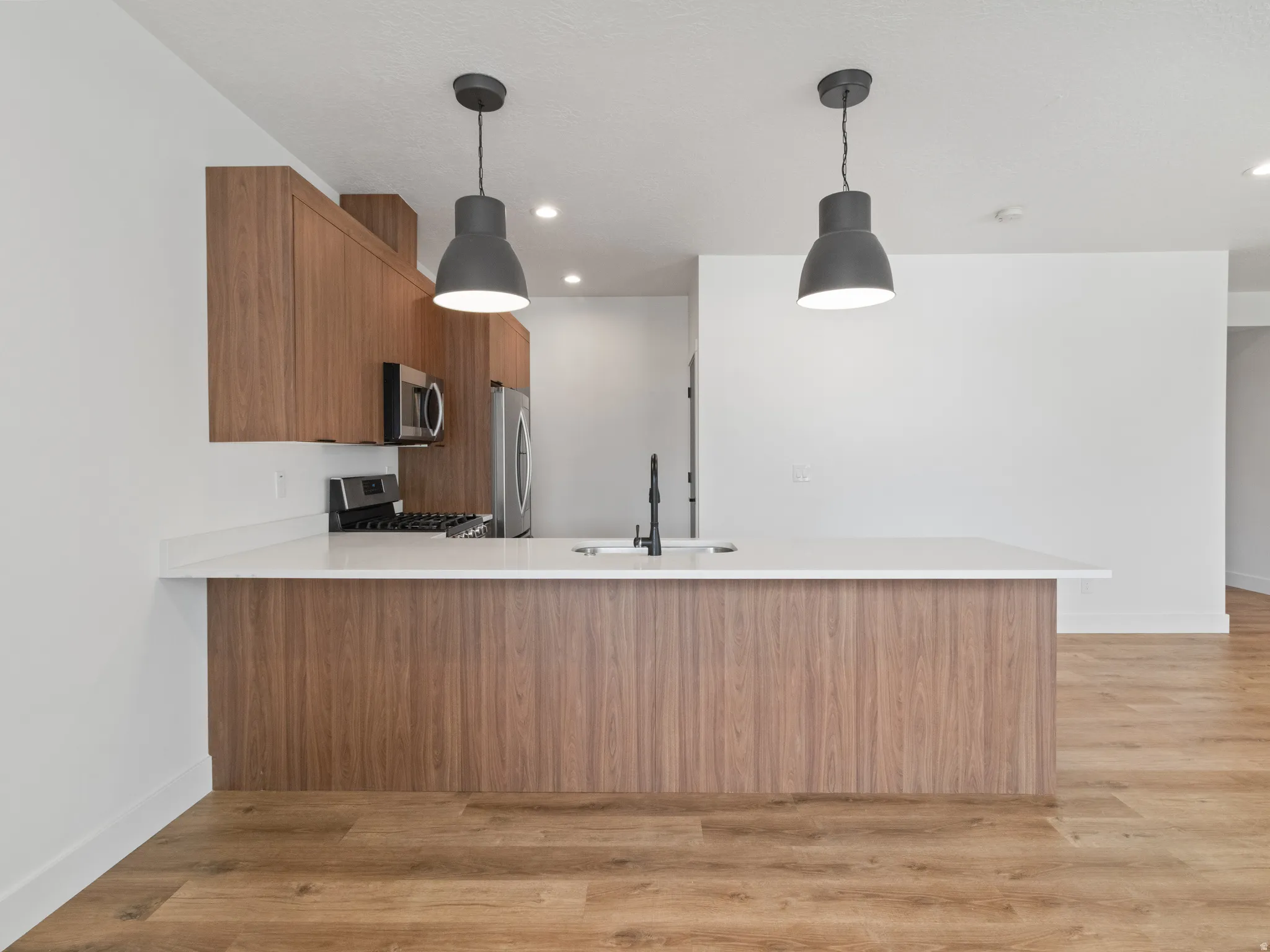 Kitchen featuring wood finish cabinets, a peninsula, light wood-style floors, and pendant lighting