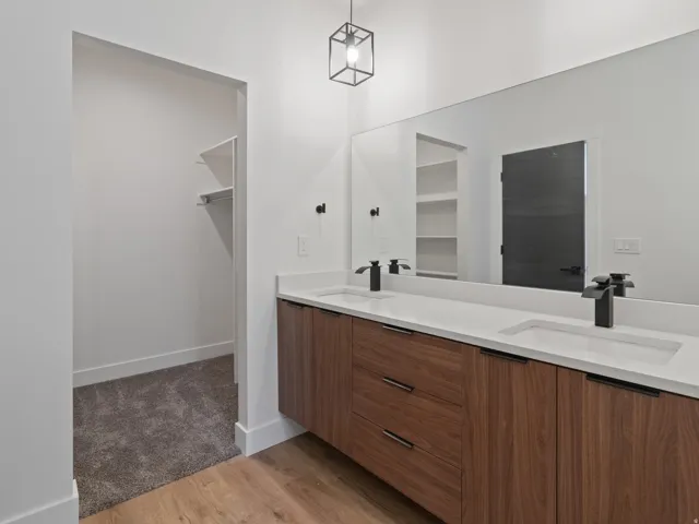 Full bathroom with double vanity, light wood finished floors, and a walk in closet