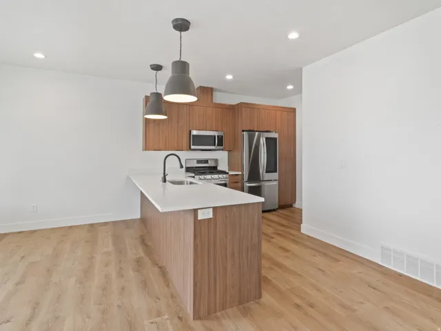 Kitchen with wood finish cabinetry, pendant lighting, modern cabinets, stainless steel appliances, and light wood-style floors