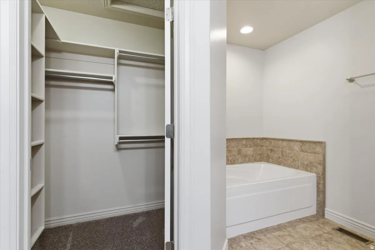 Primary Bathroom featuring a bath, a spacious closet, light tile patterned floors, and recessed lighting