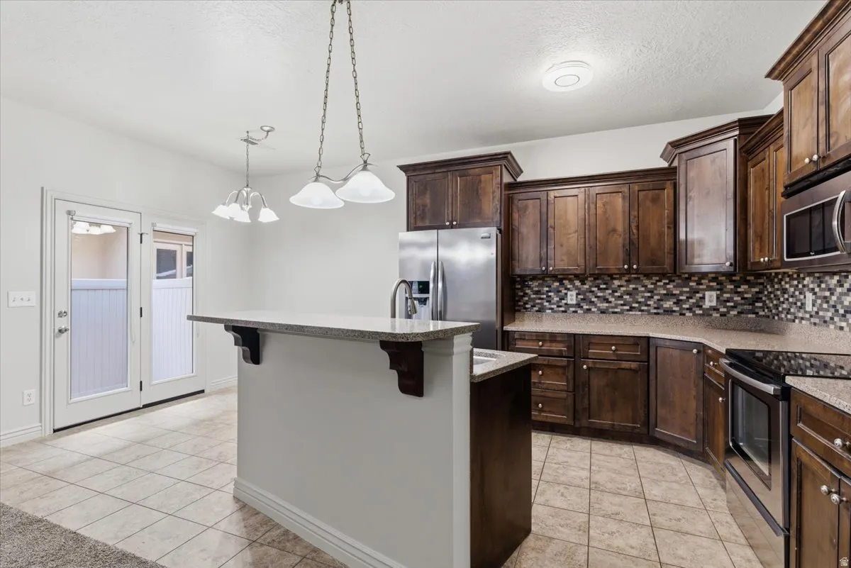 Kitchen featuring dark wood finish cabinetry, stainless steel appliances, light tile patterned floors, and a textured ceiling