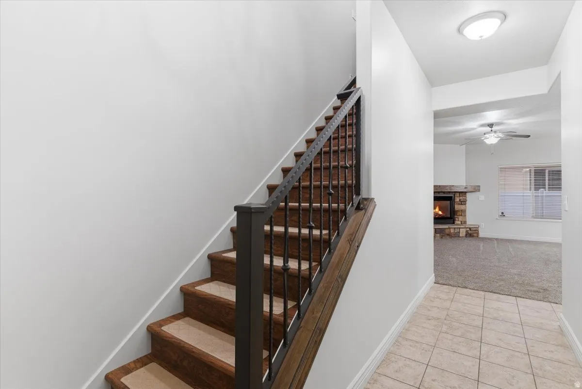 Staircase featuring a fireplace, tile patterned flooring, carpet flooring, and a ceiling fan