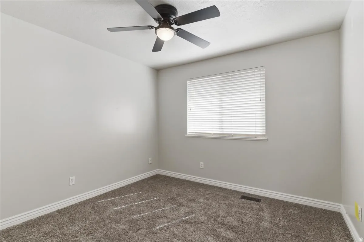 Empty room featuring dark colored carpet and a ceiling fan