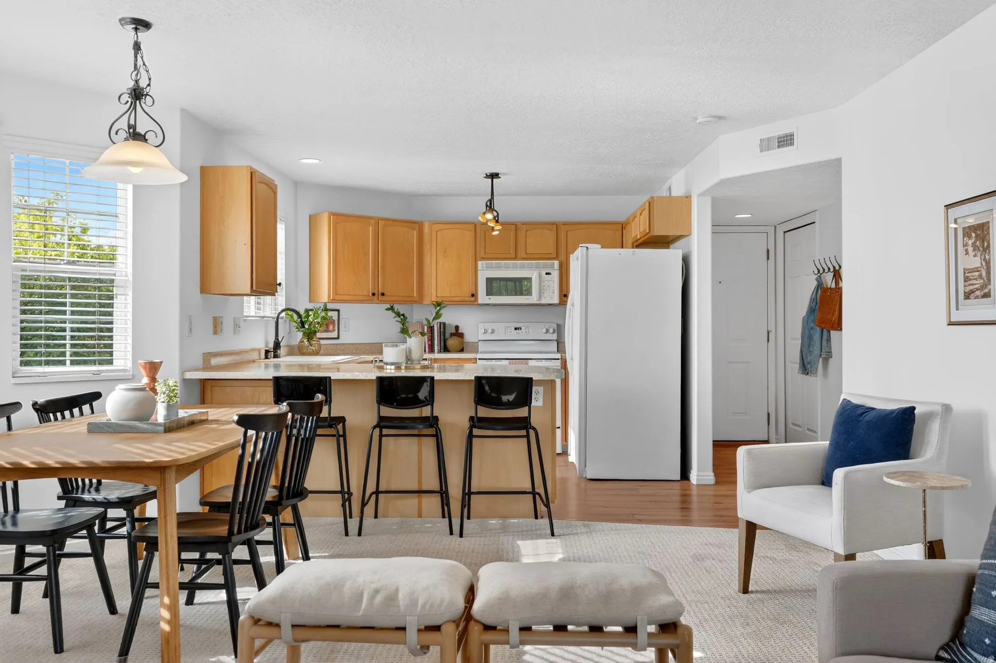 Kitchen featuring light countertops, pendant lighting, white appliances, a peninsula, and light wood-style flooring