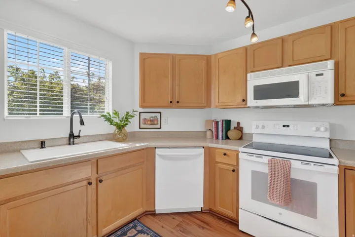 Kitchen featuring white appliances, light wood finish cabinetry, light wood finished floors, and light stone counters