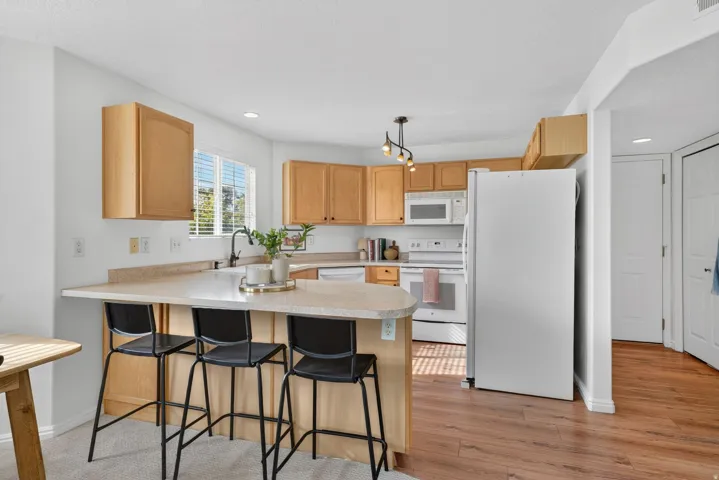Kitchen with a peninsula, white appliances, light countertops, a breakfast bar area, and decorative light fixtures