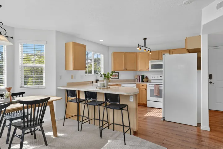 Kitchen with decorative light fixtures, white appliances, light countertops, a peninsula, and a breakfast bar area