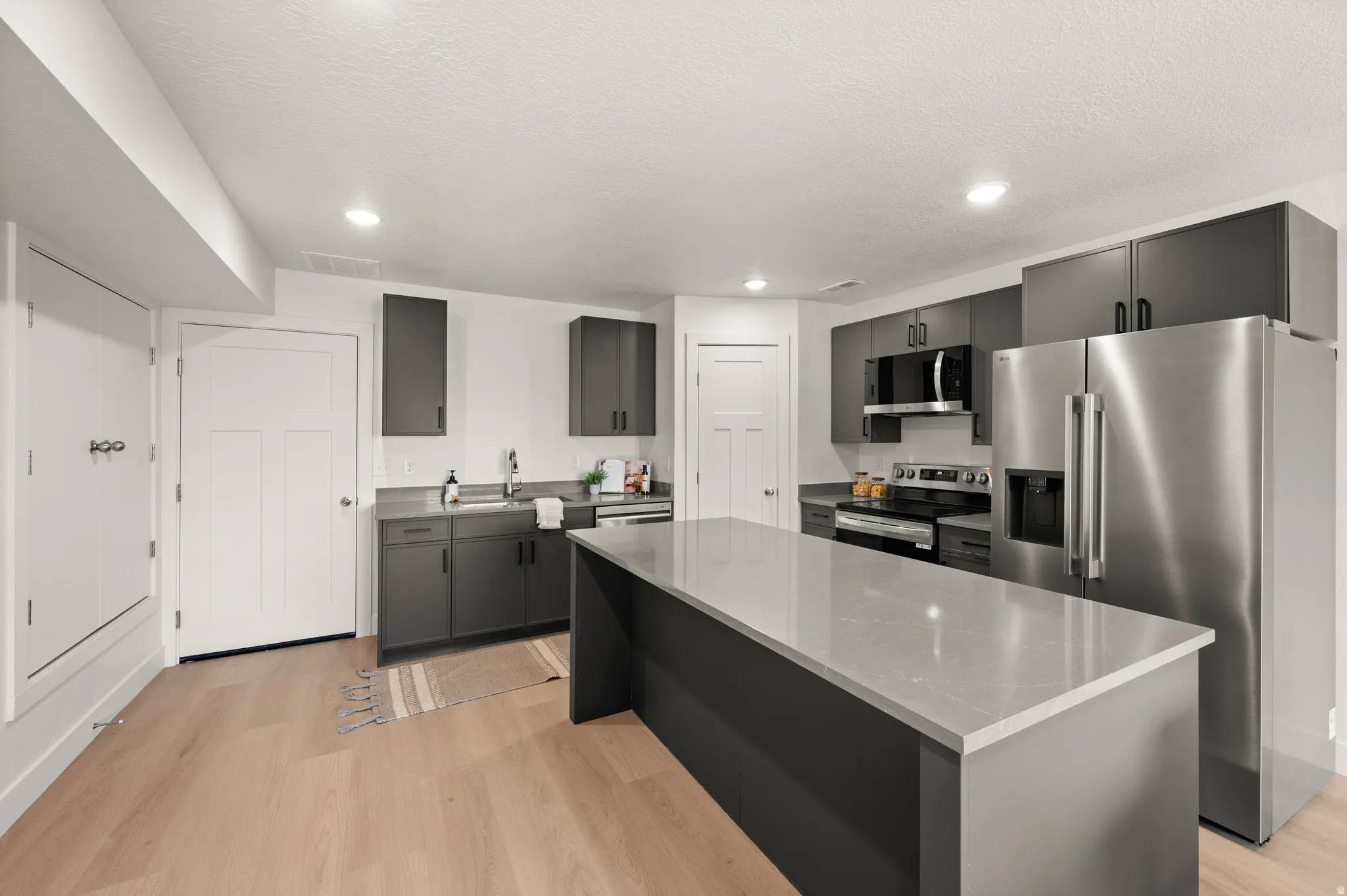 Kitchen featuring stainless steel appliances, a kitchen island, light wood-style floors, recessed lighting, and light stone countertops