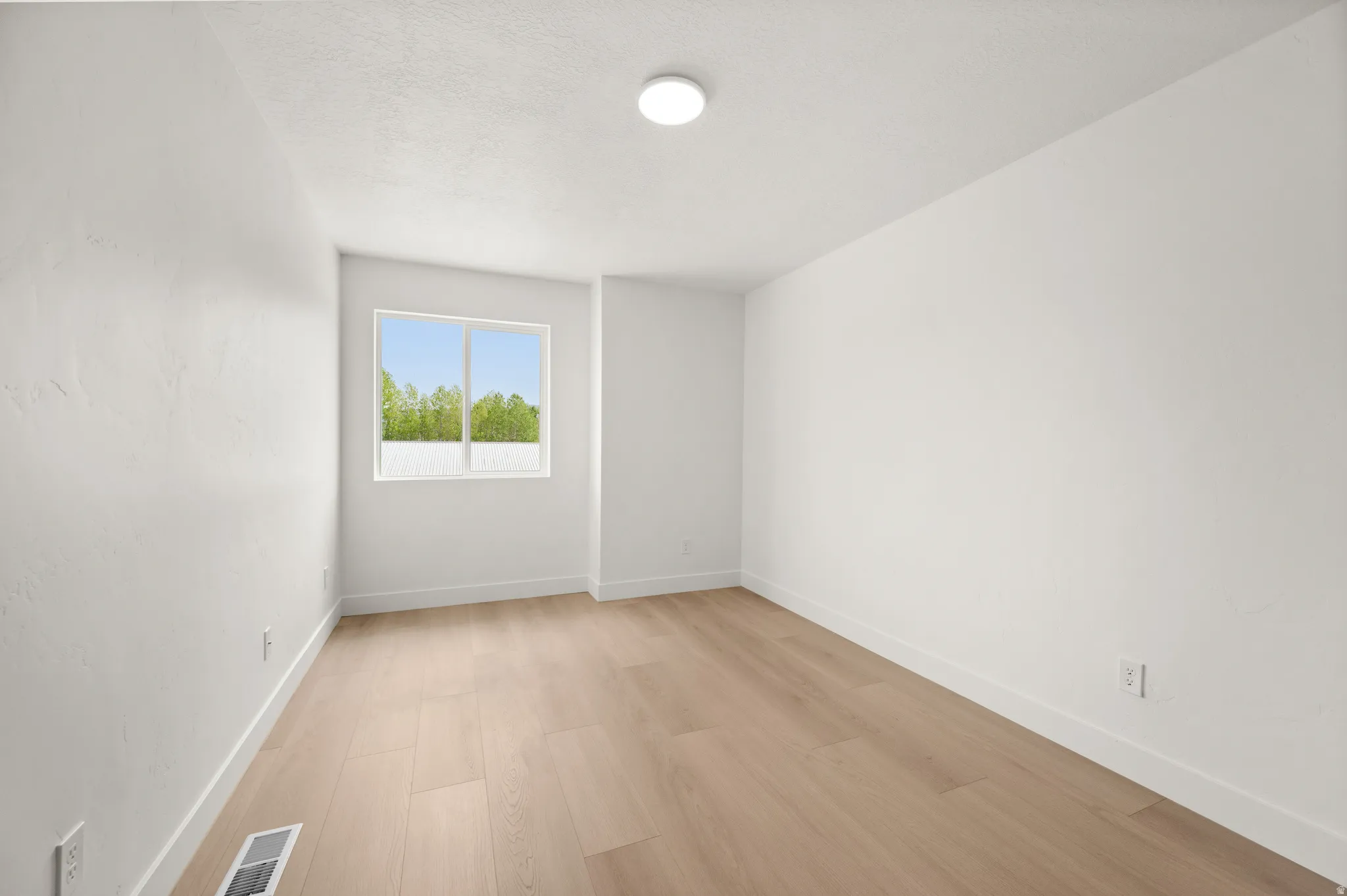 Spare room featuring light wood-type flooring and a textured ceiling