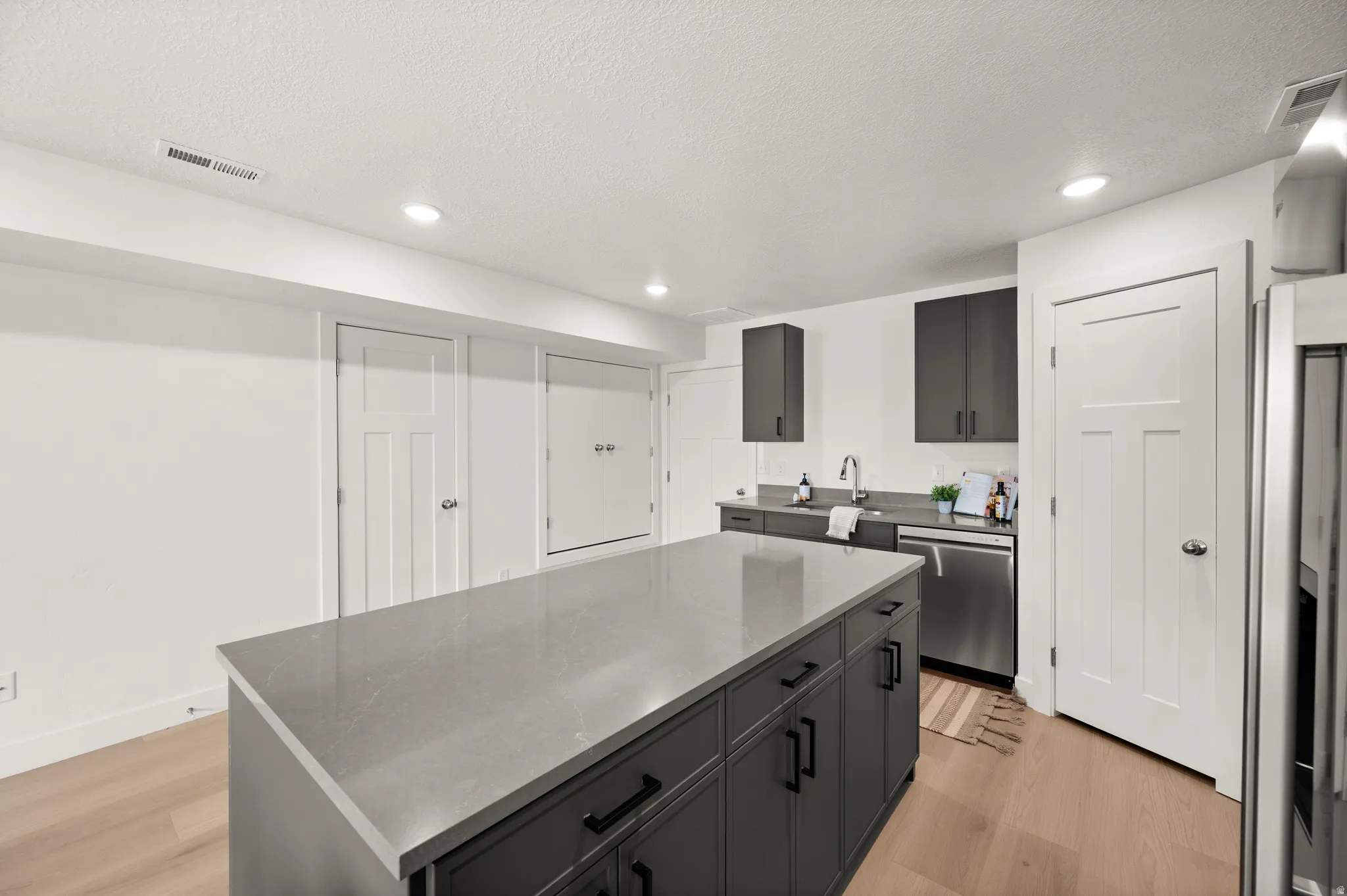 Kitchen with light wood-style floors, a kitchen island, stainless steel appliances, recessed lighting, and a textured ceiling