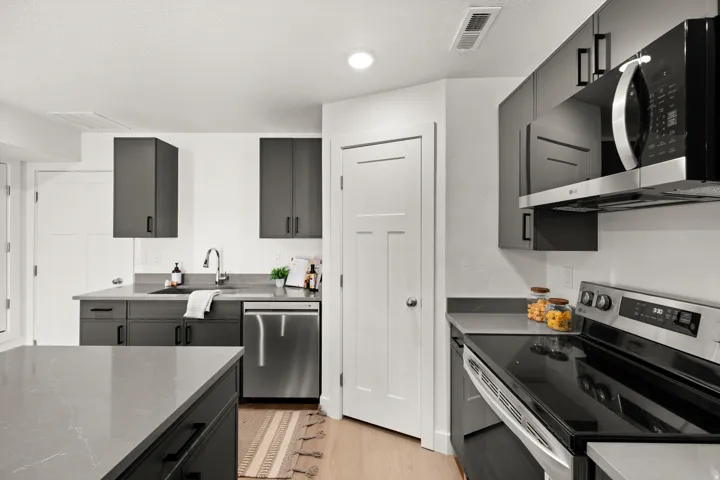 Kitchen with stainless steel appliances, dark stone counters, light wood finished floors, gray cabinetry, and a textured ceiling
