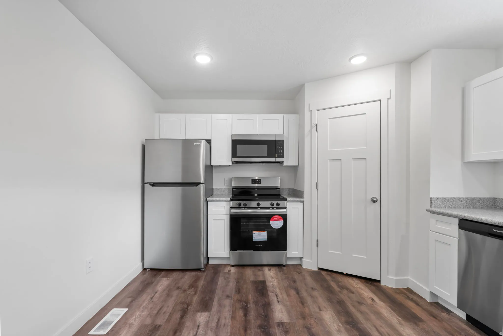 Kitchen with stainless steel appliances, white cabinets, and dark wood-type flooring