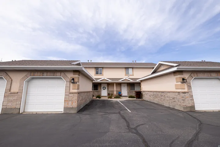 Traditional-style townhome with single car garages, stucco siding, covered porch, stone siding, and a shingled roof
