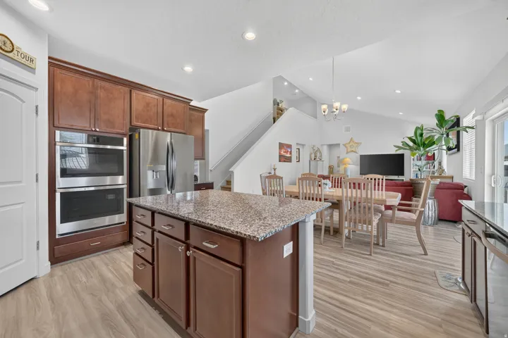 Open-concept living area featuring a kitchen island with stone-finish countertop, wood-finish flooring, stainless steel double ovens, and a refrigerator